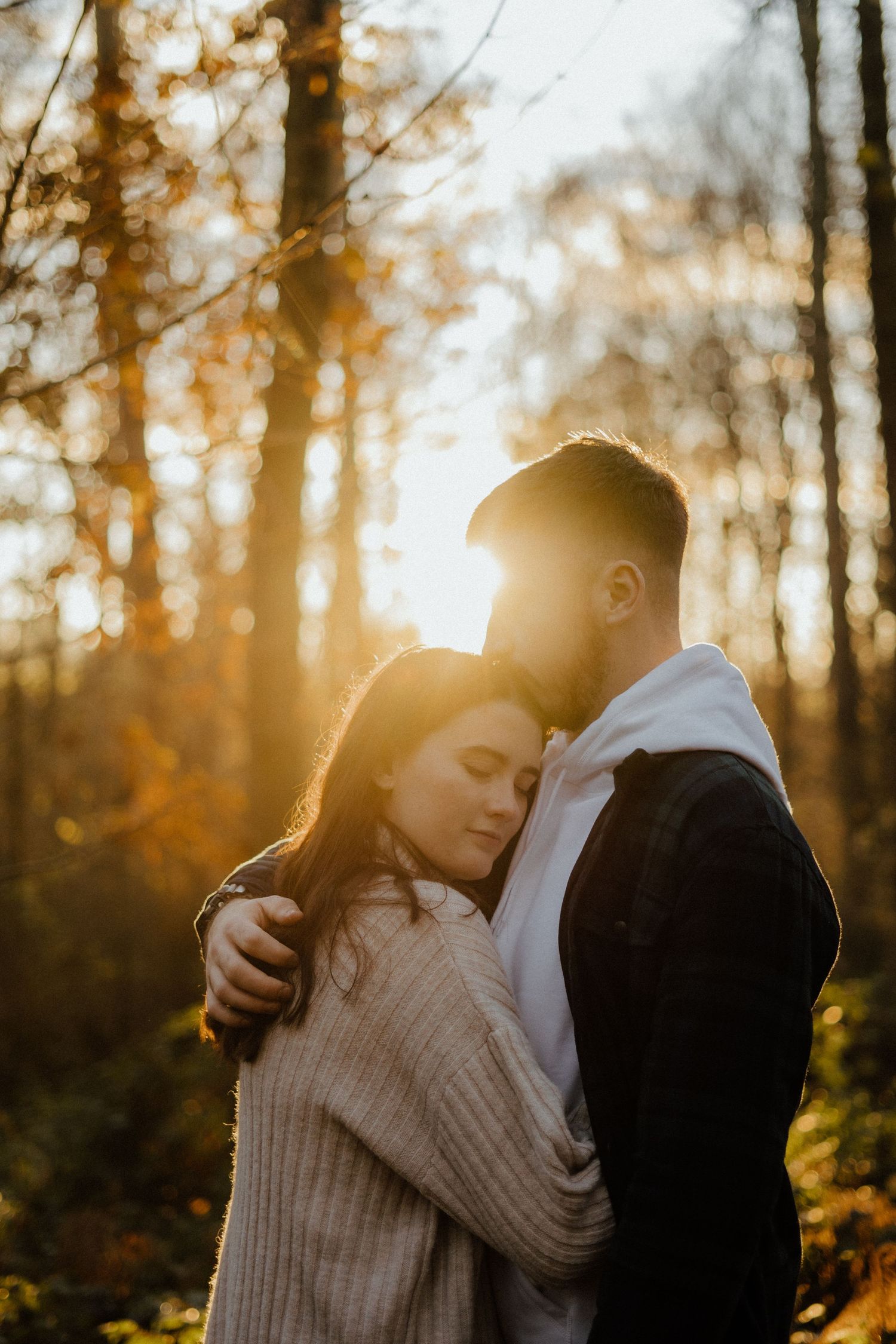 Couple sharing tender embrace in glowing autumn forest during golden hour sunset.