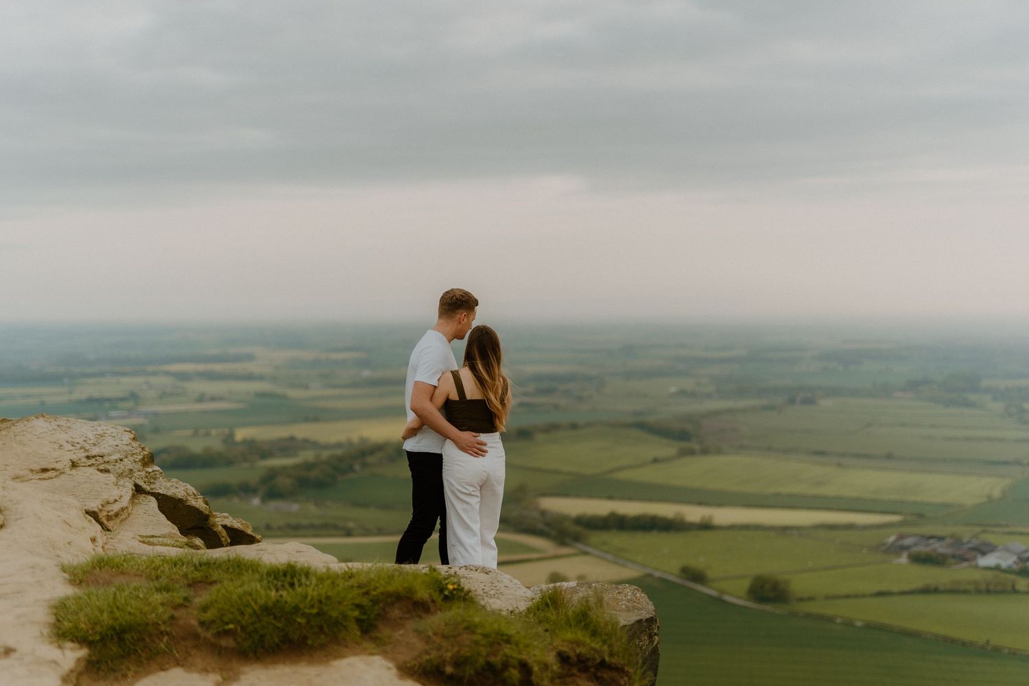 Romantic couple embracing on a rocky hilltop with sweeping green valley views.