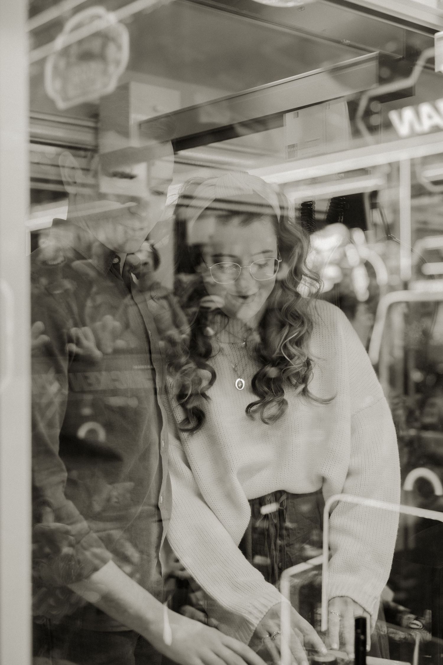 Black and white photo of woman with curly hair reflected in arcade game glass window.