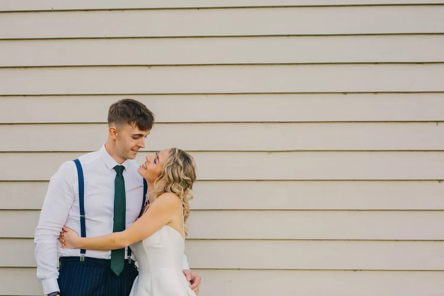 A romantic wedding portrait against a white siding wall.