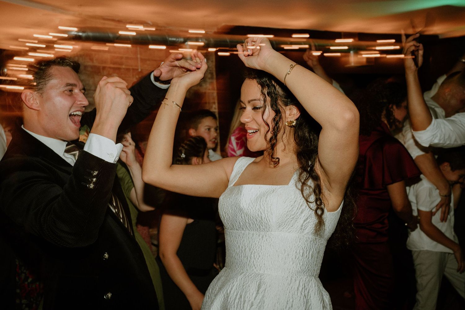 Bride and groom dancing joyfully together with raised hands at their wedding reception.