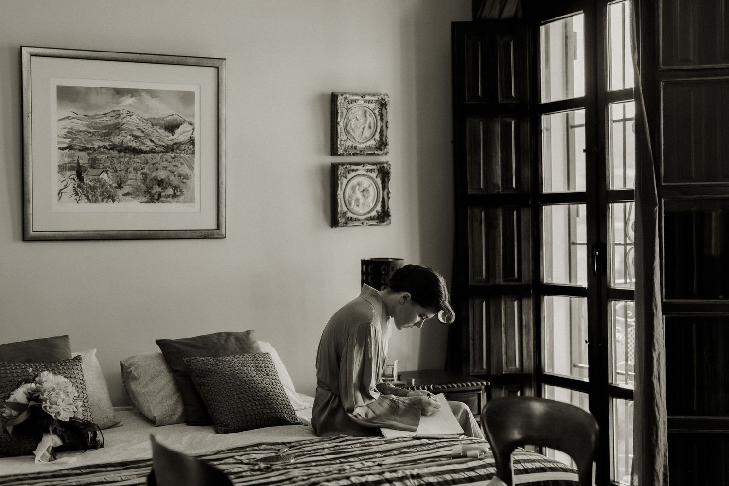 Black and white photo of bride getting ready in elegant room beside tall wooden doors.