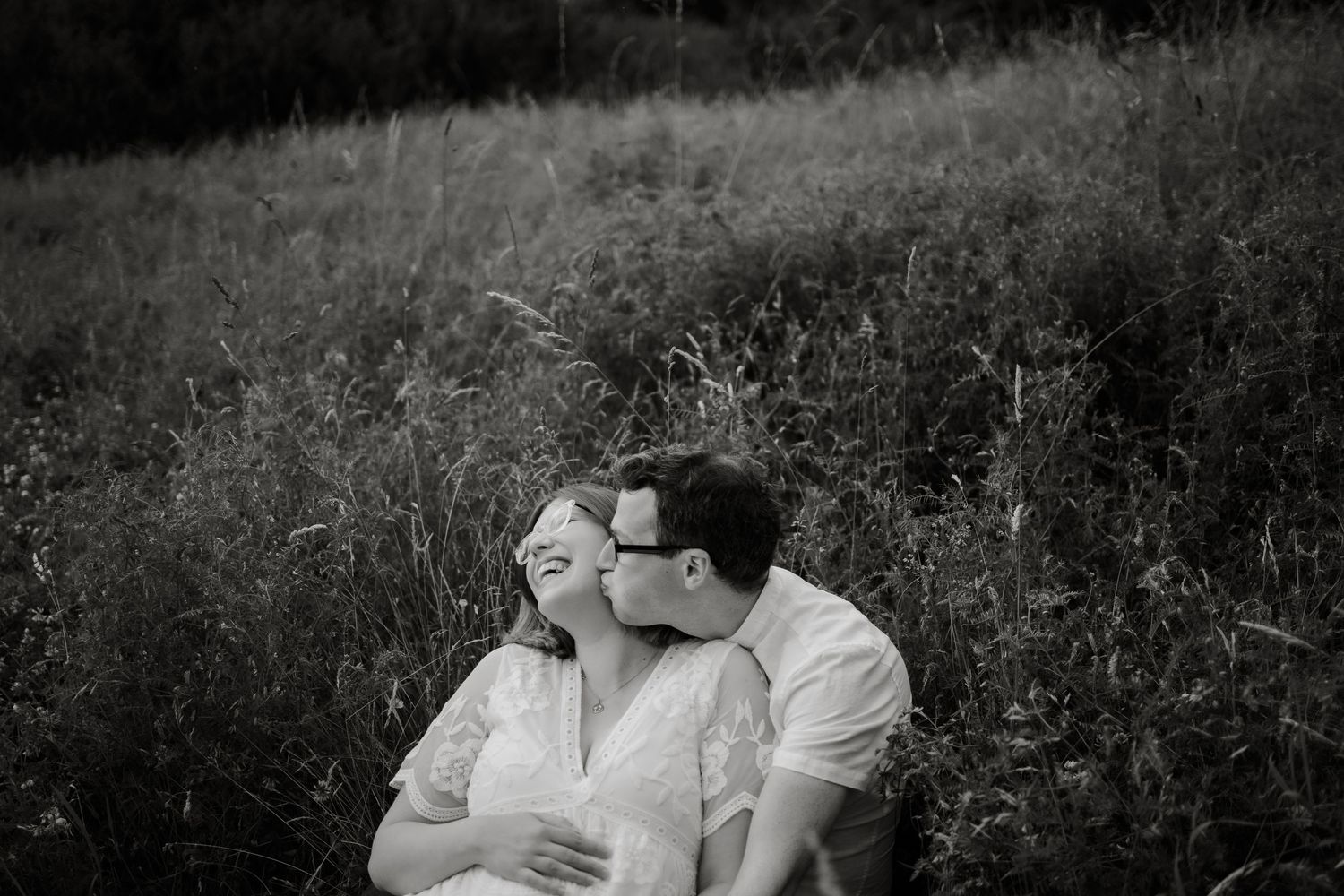 A black and white photo of a couple sitting in a meadow, sharing a tender moment.