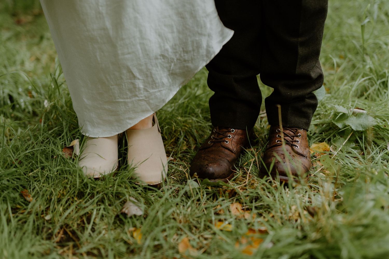 Wedding shoes of a couple standing together on grass, showing white and brown leather footwear.