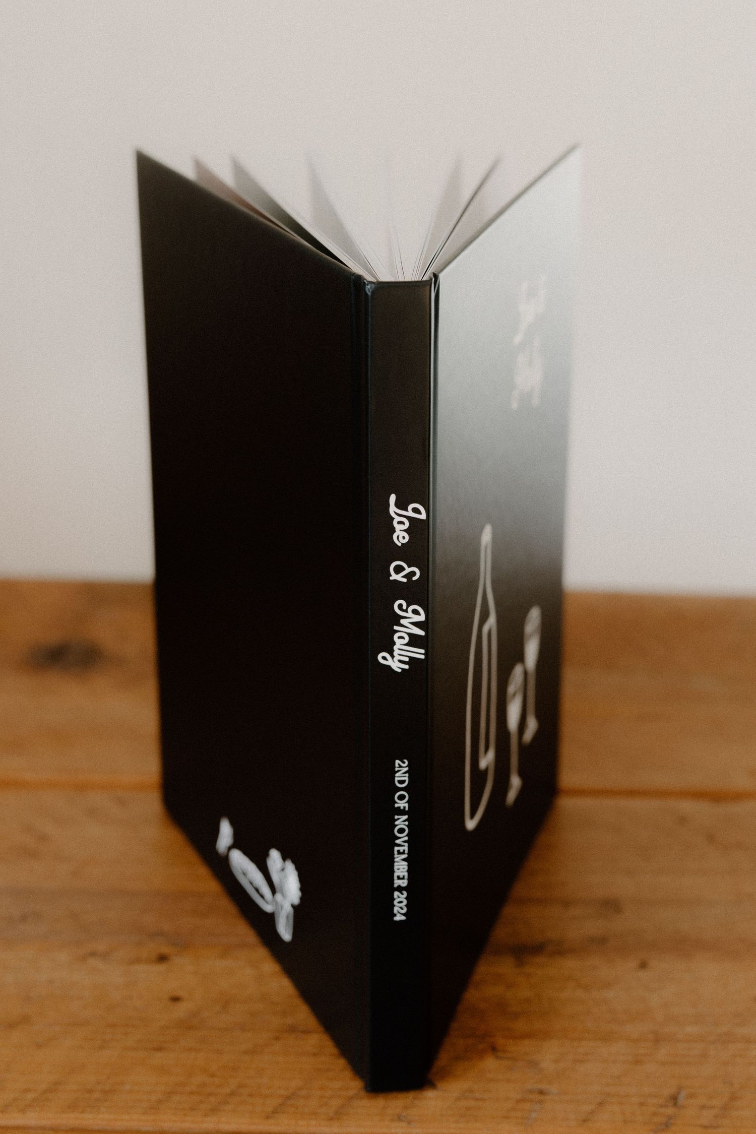 An open black book standing upright on a wooden surface, with pages fanned out creating a radial pattern.