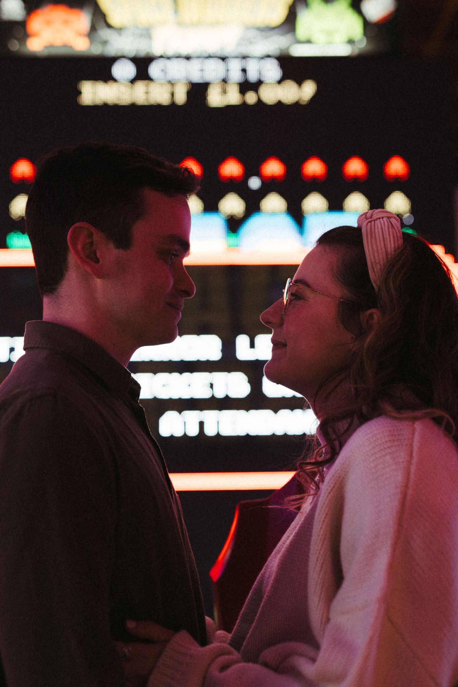Romantic couple gazing into each other's eyes in front of colorful arcade game neon lights.