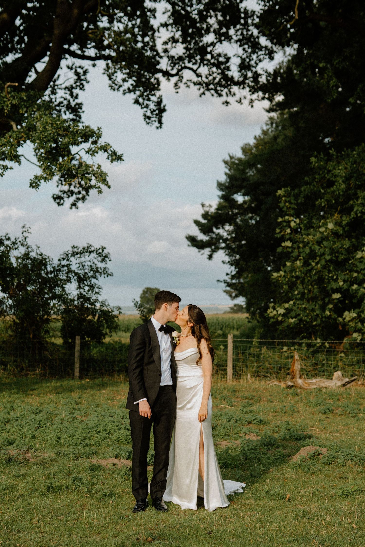 Bride and groom kissing in a lush green countryside setting on their wedding day.