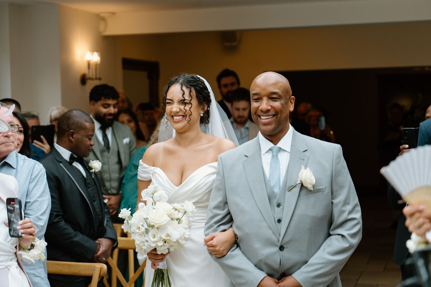 Bride in off-shoulder gown walks down the aisle with her proud father.