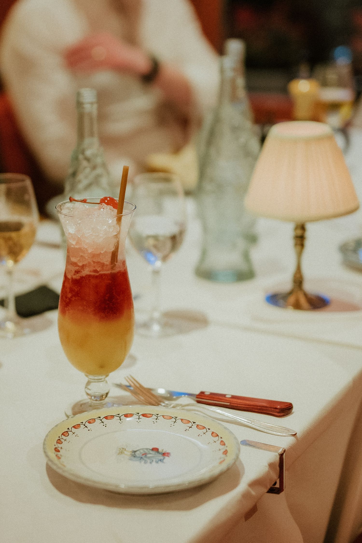 A vibrant Tequila Sunrise cocktail with ice on an elegant restaurant table set with fine china and glassware.
