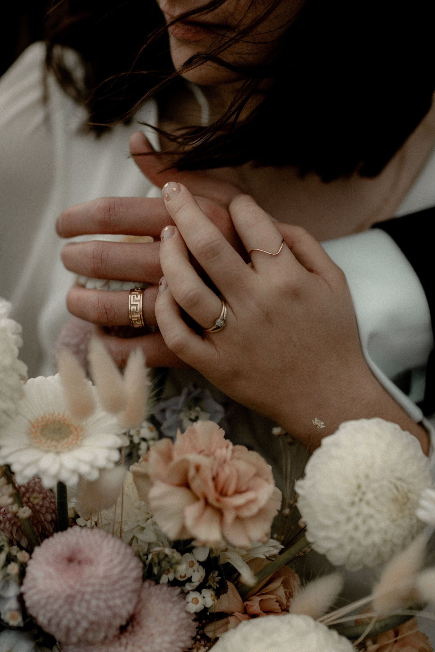 Close-up of wedding rings and hands with soft pink and white flowers.