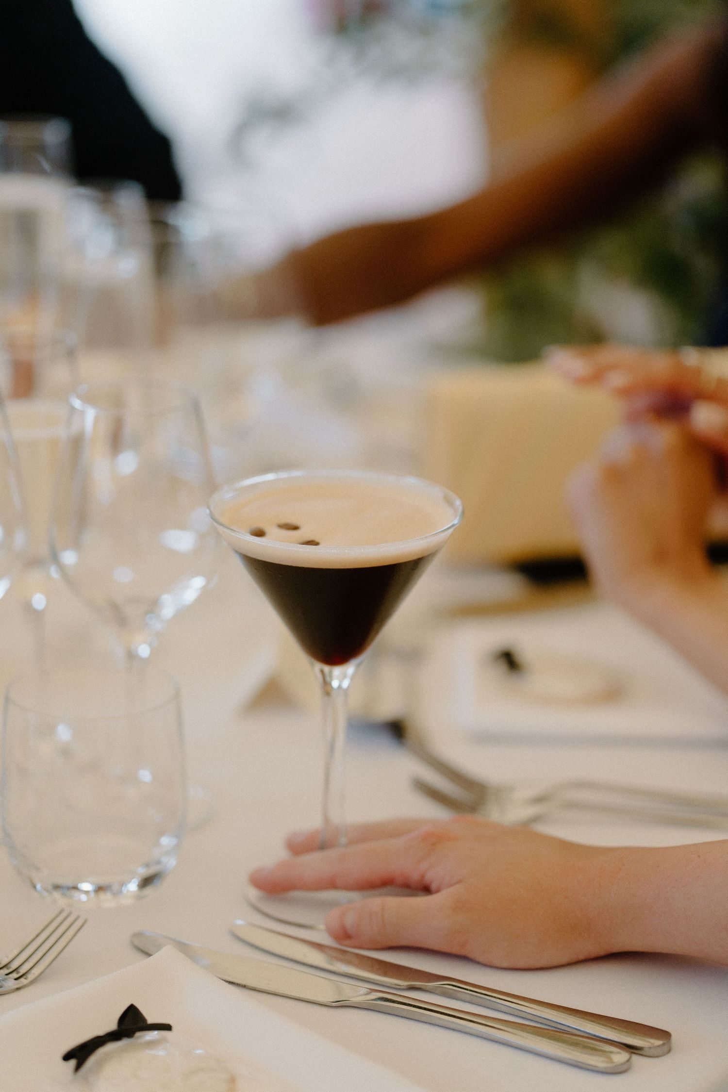 Espresso martini cocktail in a martini glass on a white linen wedding reception table setting.