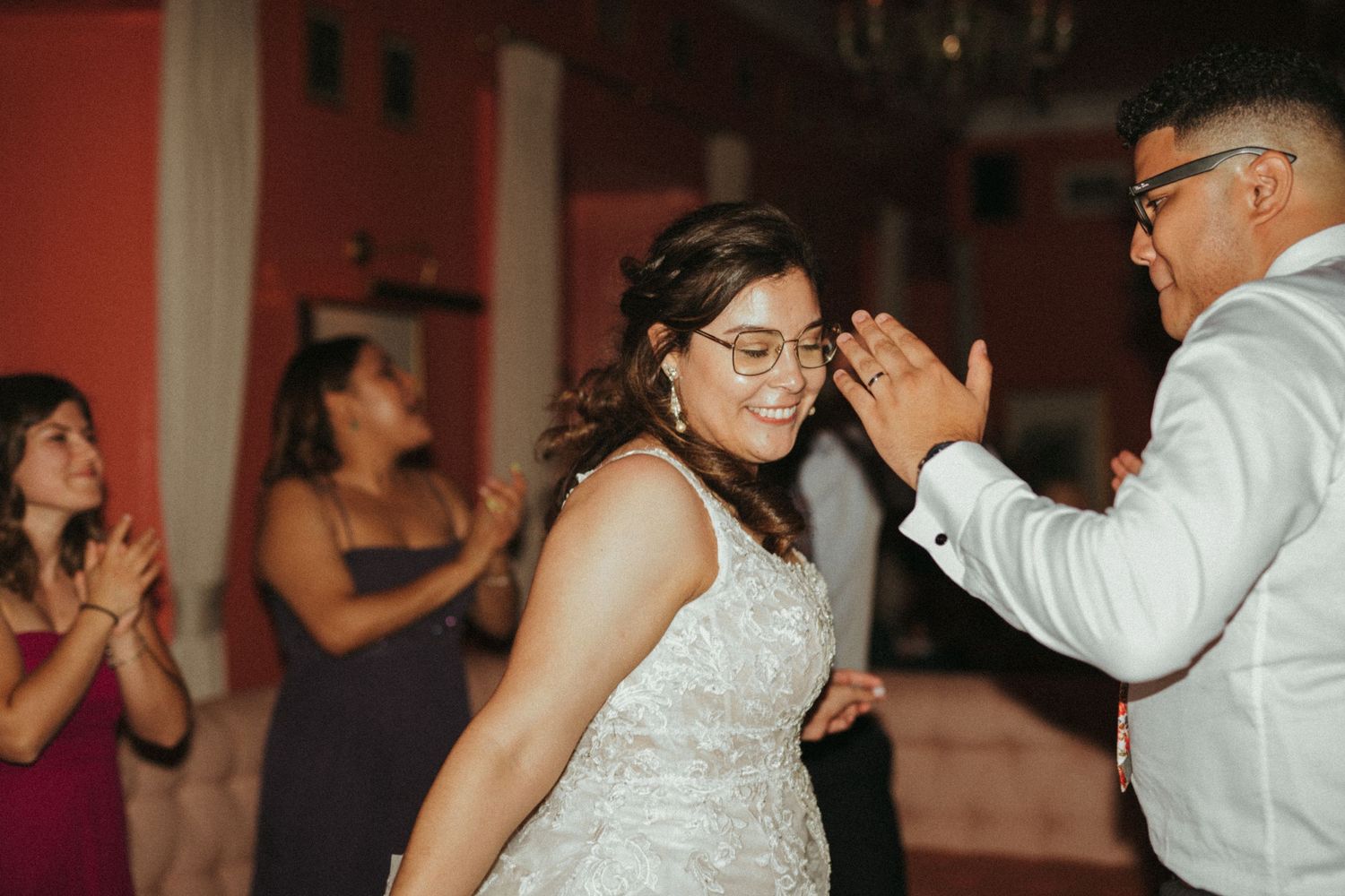 Bride in lace wedding gown laughing joyfully while dancing with a guest at her wedding reception.