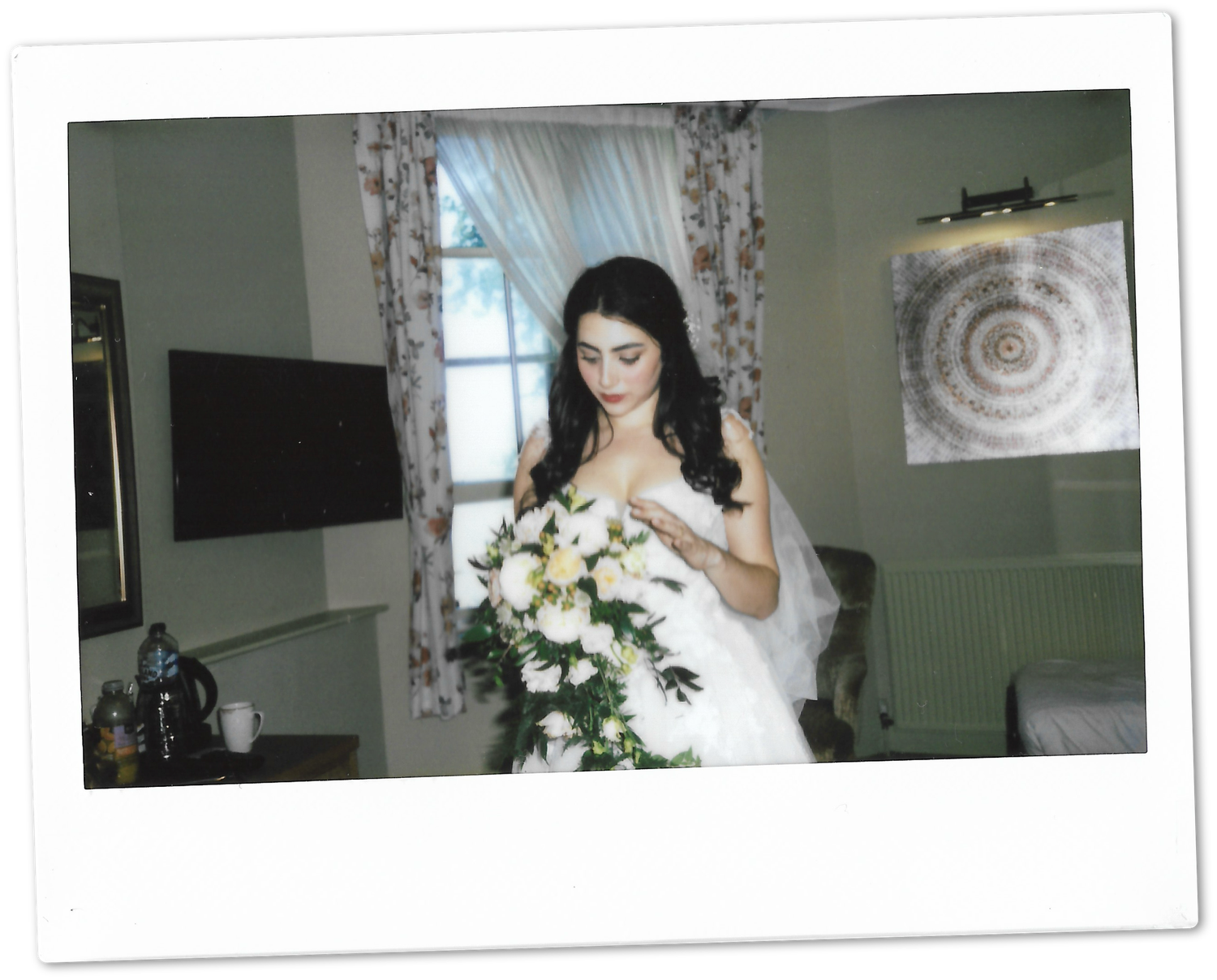 Bride in white wedding gown holding large white floral bouquet in a softly lit room.