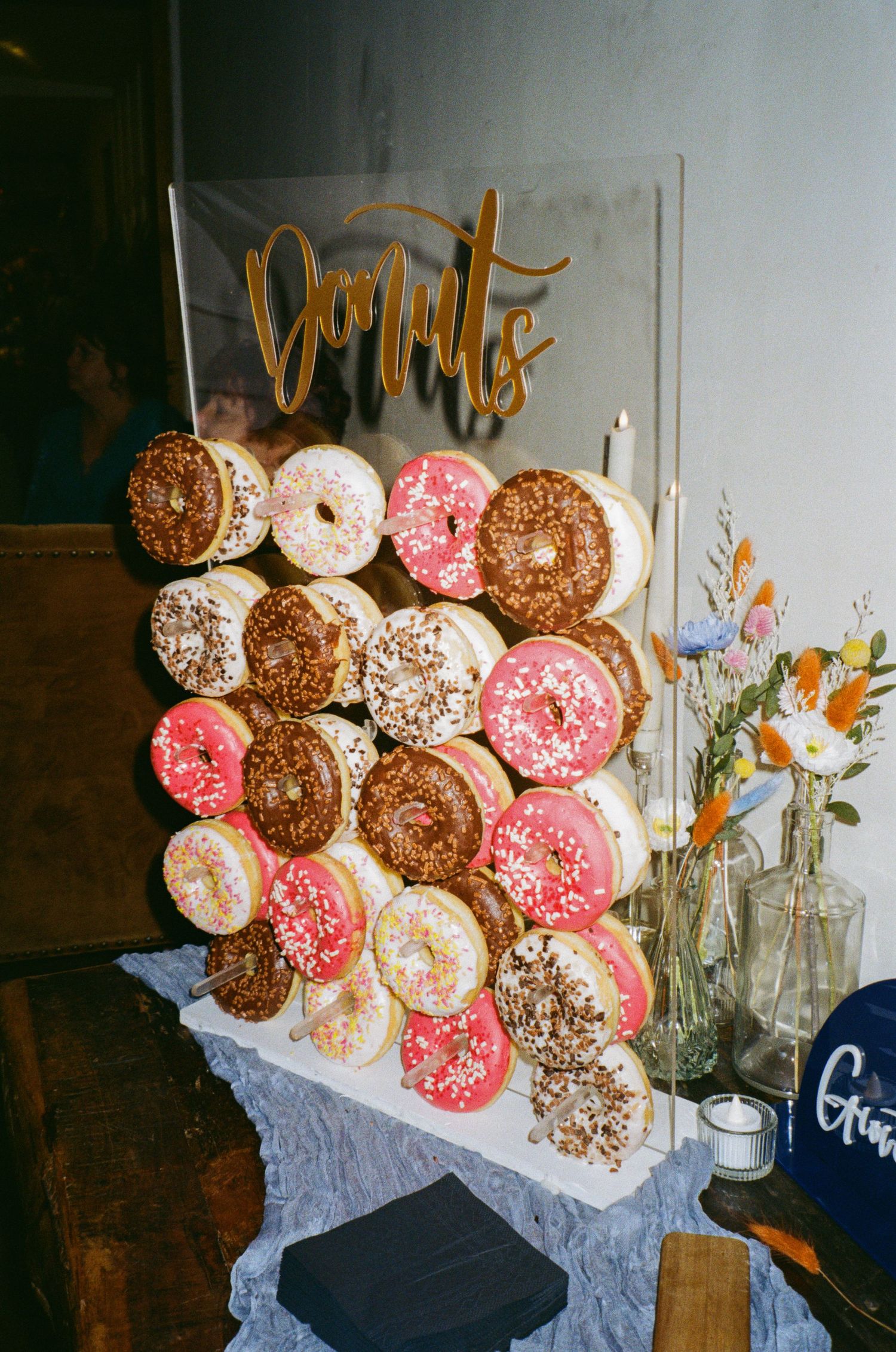 A donut wall display featuring pink, chocolate, and vanilla frosted donuts decorated with sprinkles next to small flower vases.