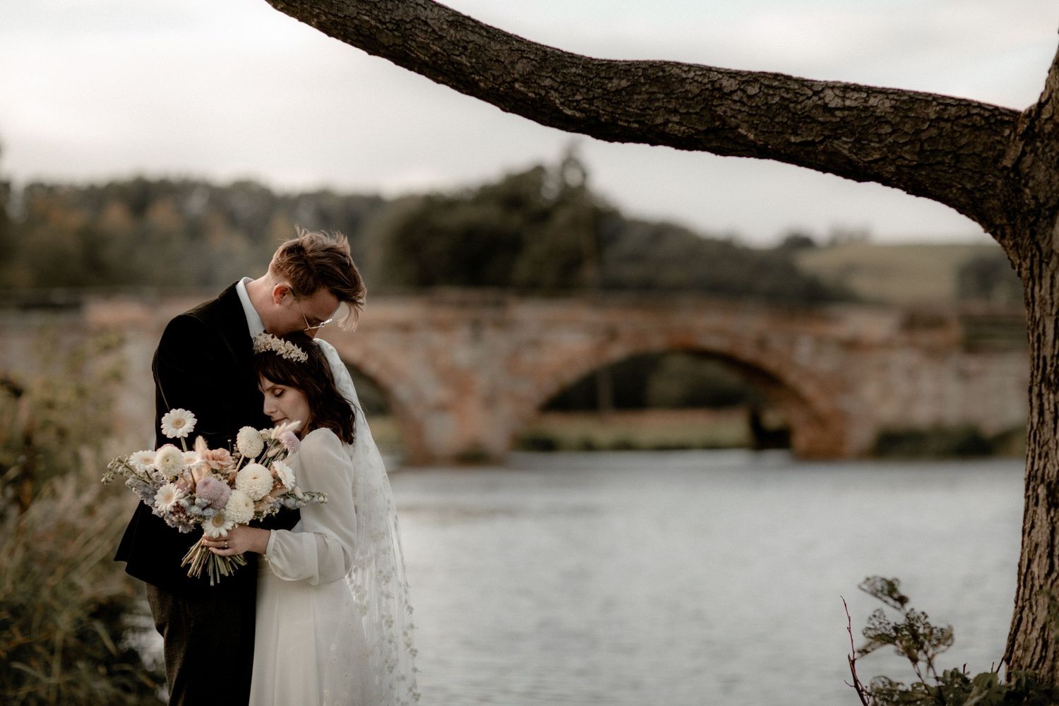 A scenic wedding photo featuring a stone bridge and river backdrop.