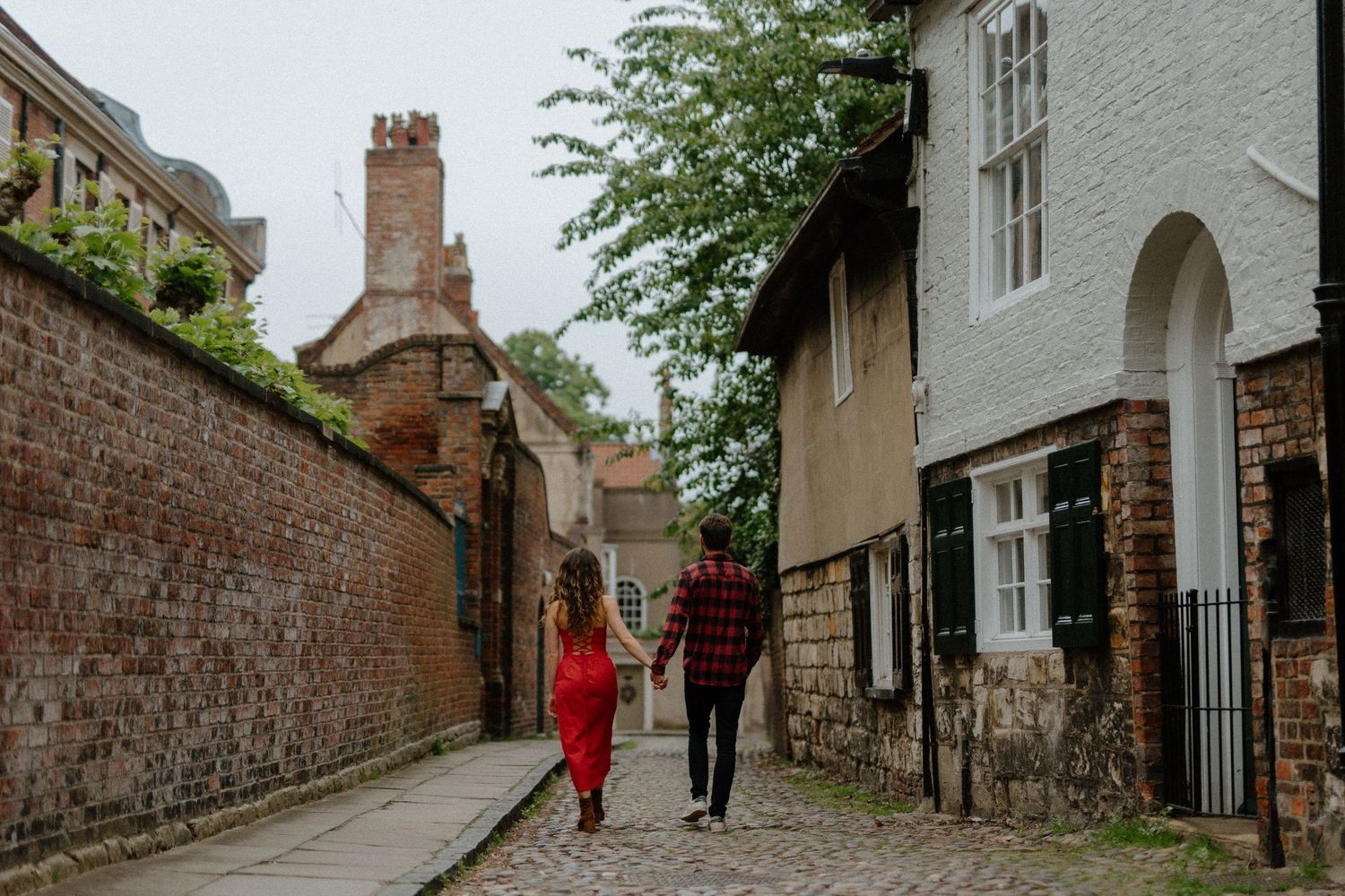 Couple walking hand in hand down a charming cobblestone alley lined with brick buildings.
