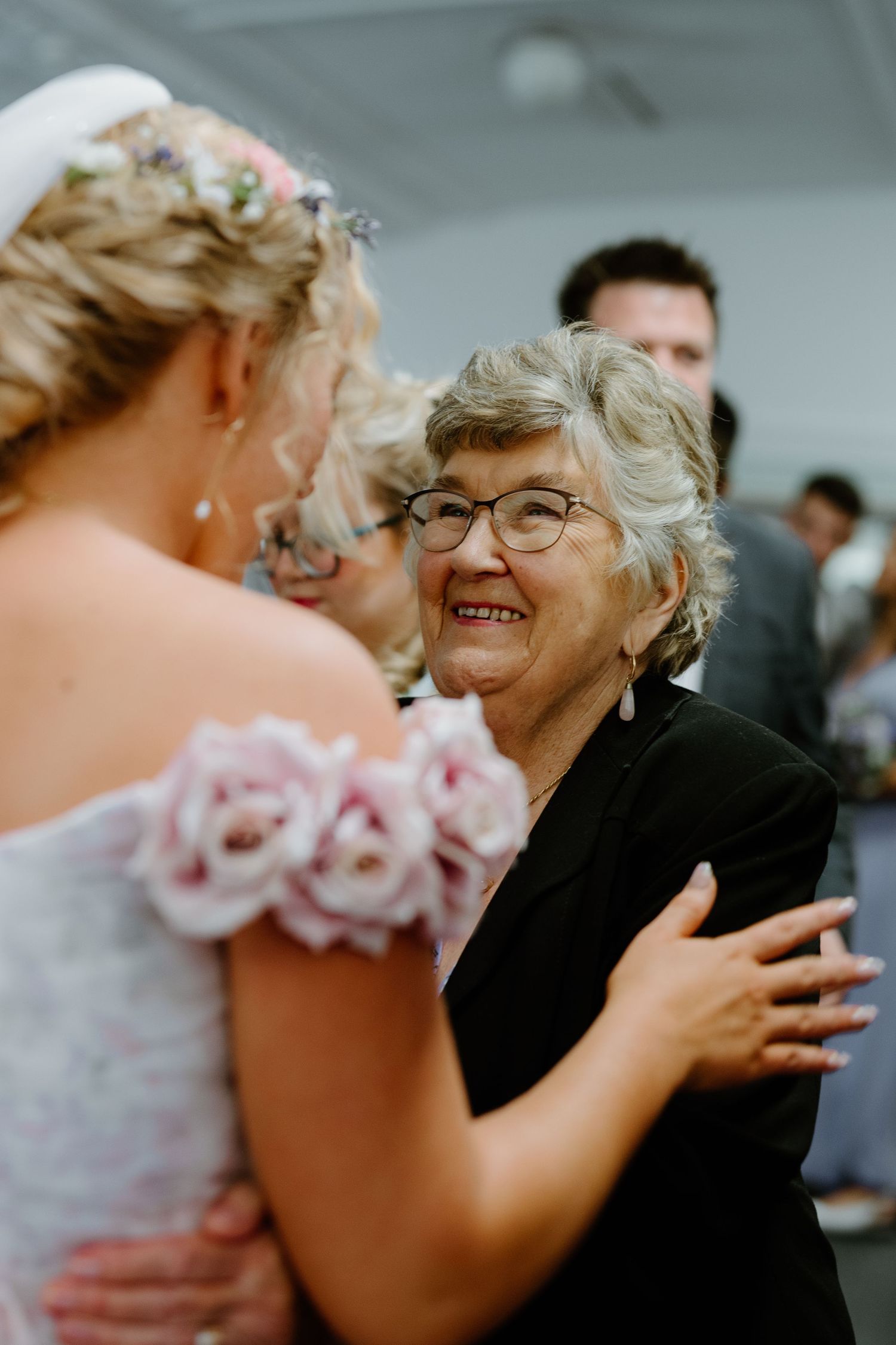 Elderly grandmother smiles warmly while embracing the bride at a wedding reception.