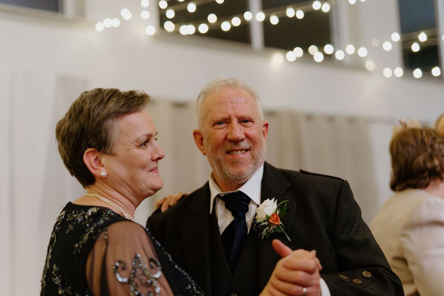 Elderly couple sharing a sweet dance together at a wedding reception with fairy lights glowing behind them.