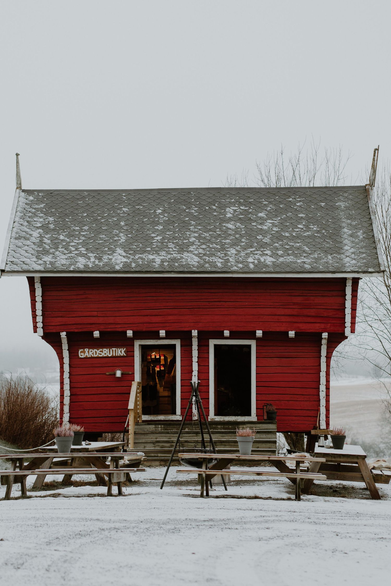 Small red wooden building with snow-covered roof and picnic tables outside stands against a winter landscape.