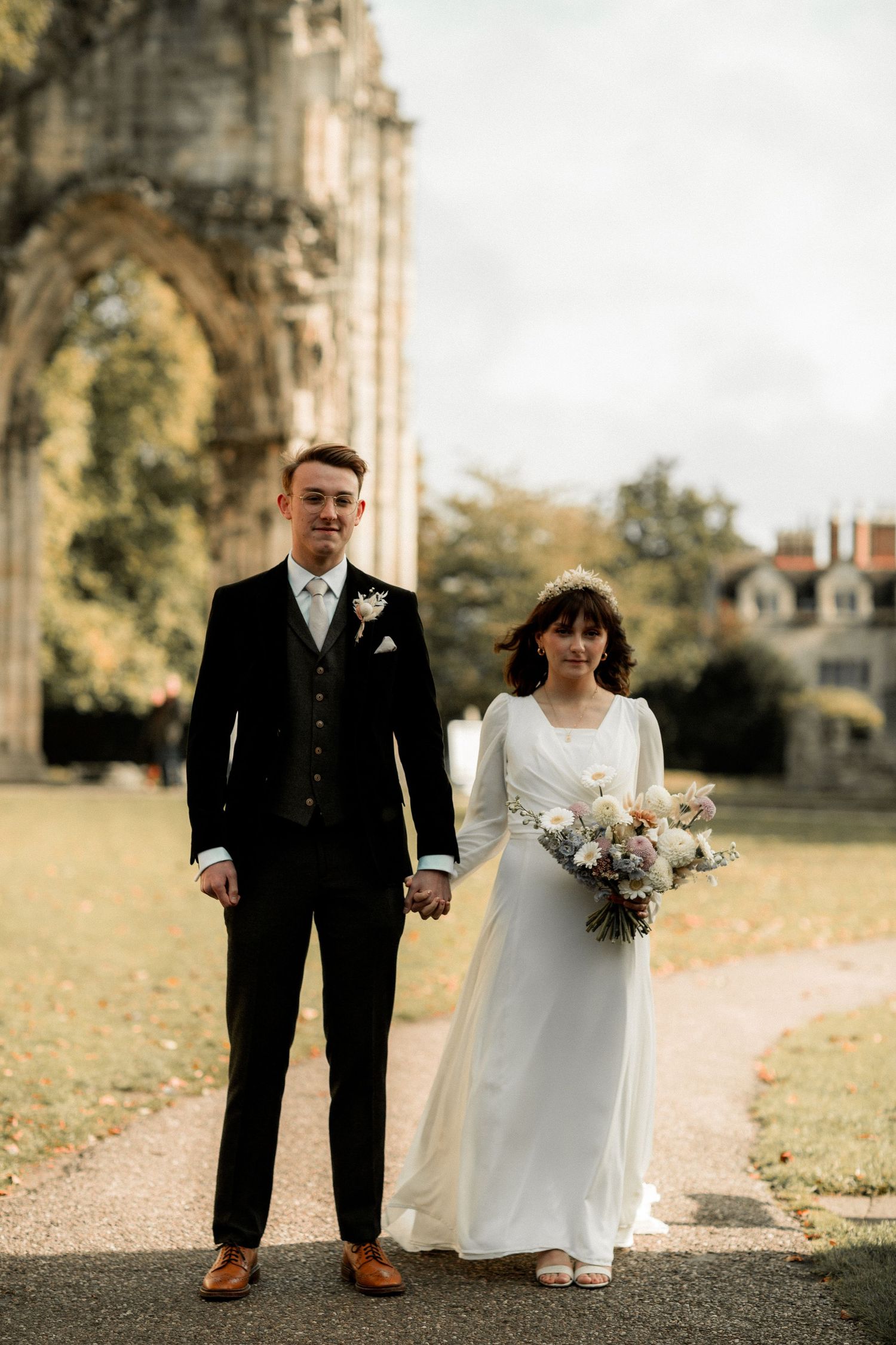 Elegant wedding couple standing on pathway with gothic architecture in background.