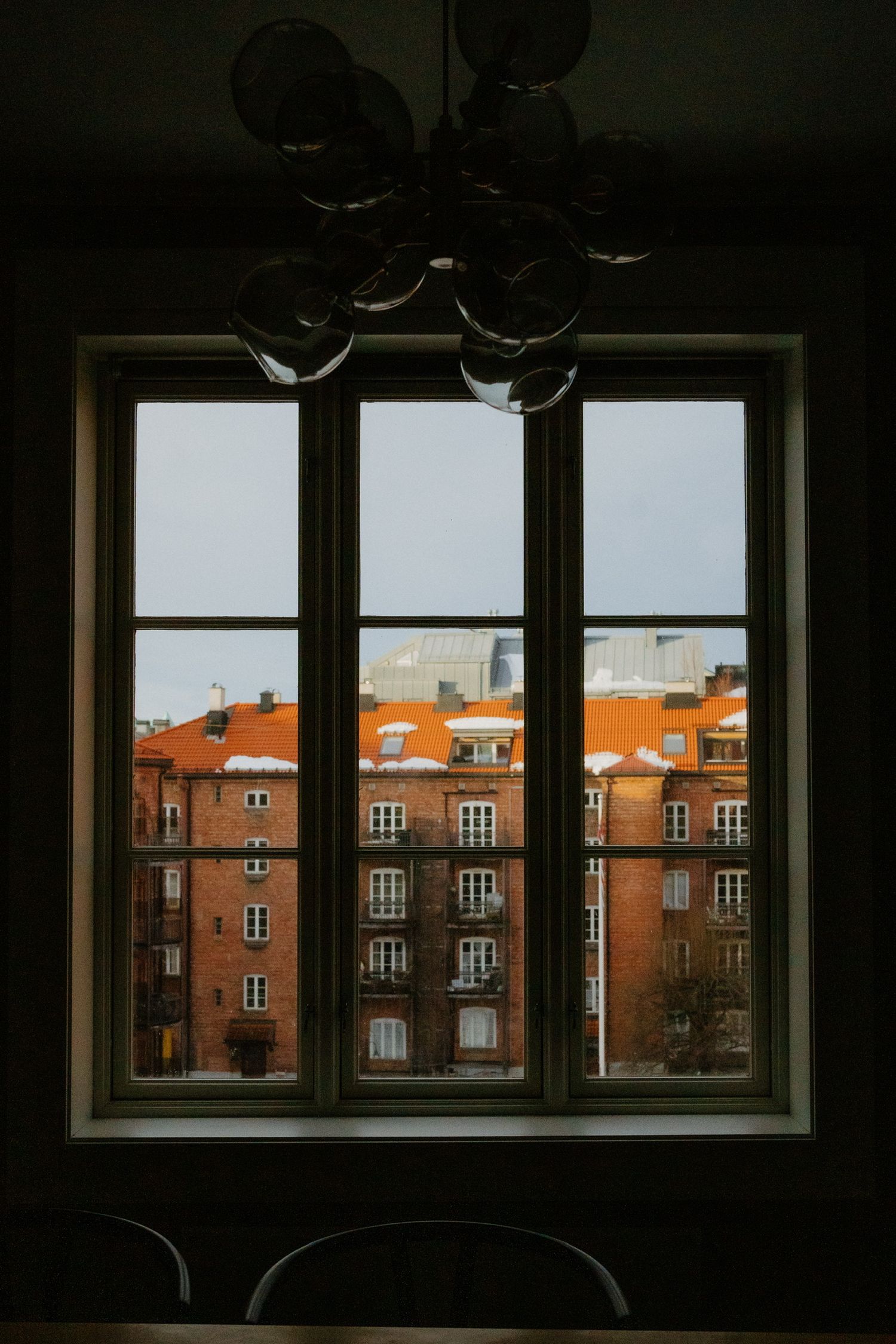Window view of orange brick apartment buildings with vintage light fixtures hanging above.