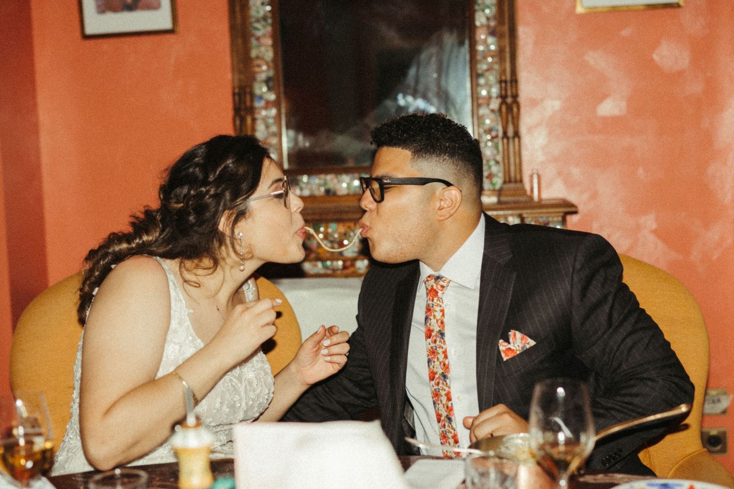 A couple shares a playful moment while dining at a restaurant with orange walls and ornate decor.