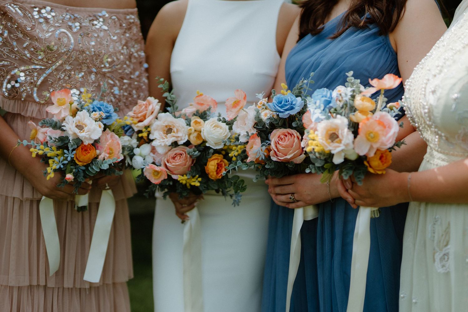 Close-up of bridesmaids holding vibrant pink, orange, and blue wedding bouquets in pastel dresses.