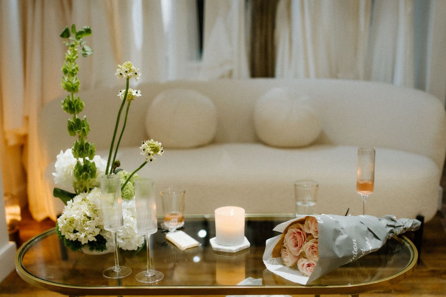 Elegant living room vignette with white floral arrangements, glowing candles, and plush cream sofa in soft lighting.