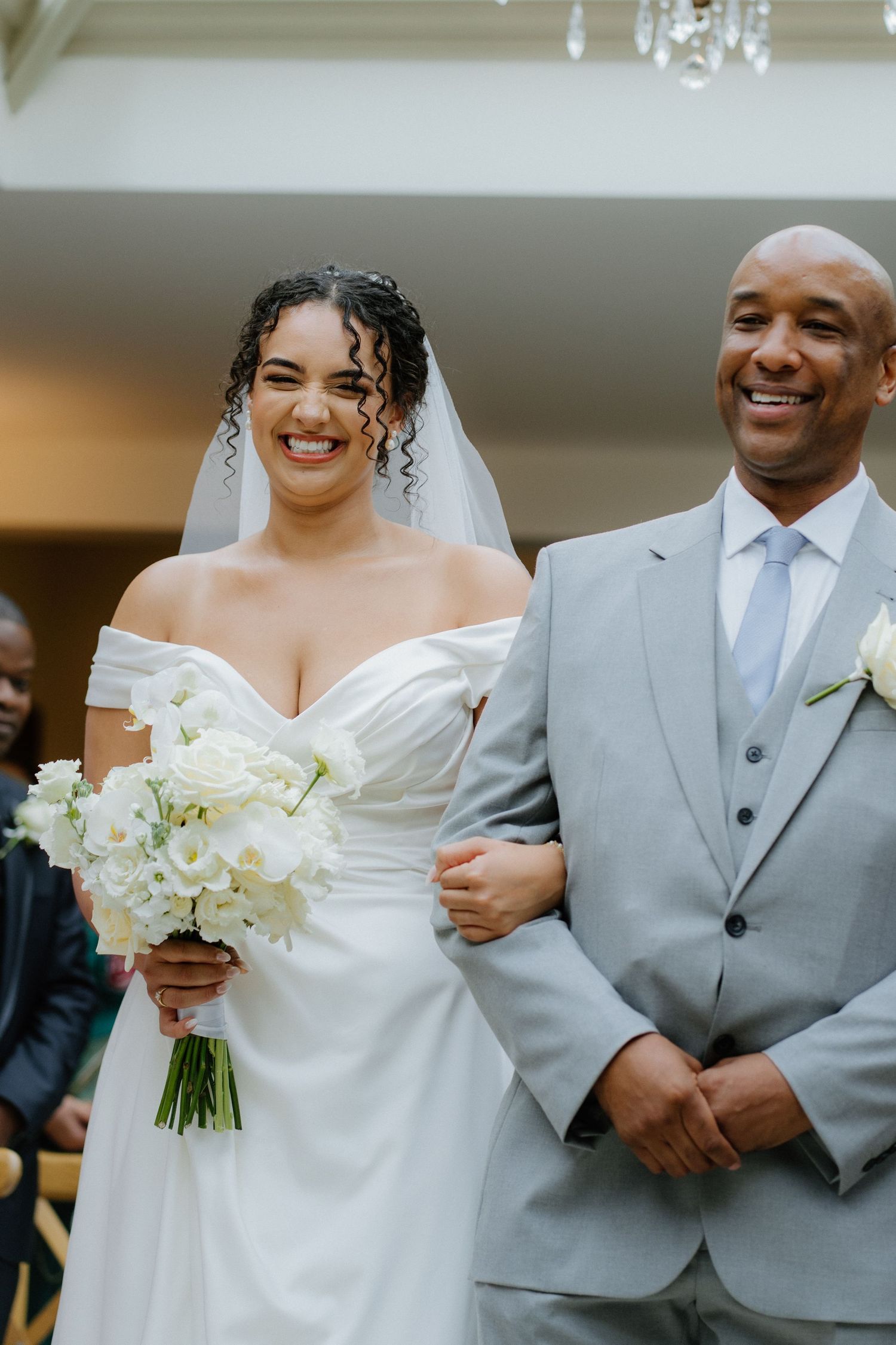 Radiant bride walking down the aisle with her father holding white roses.