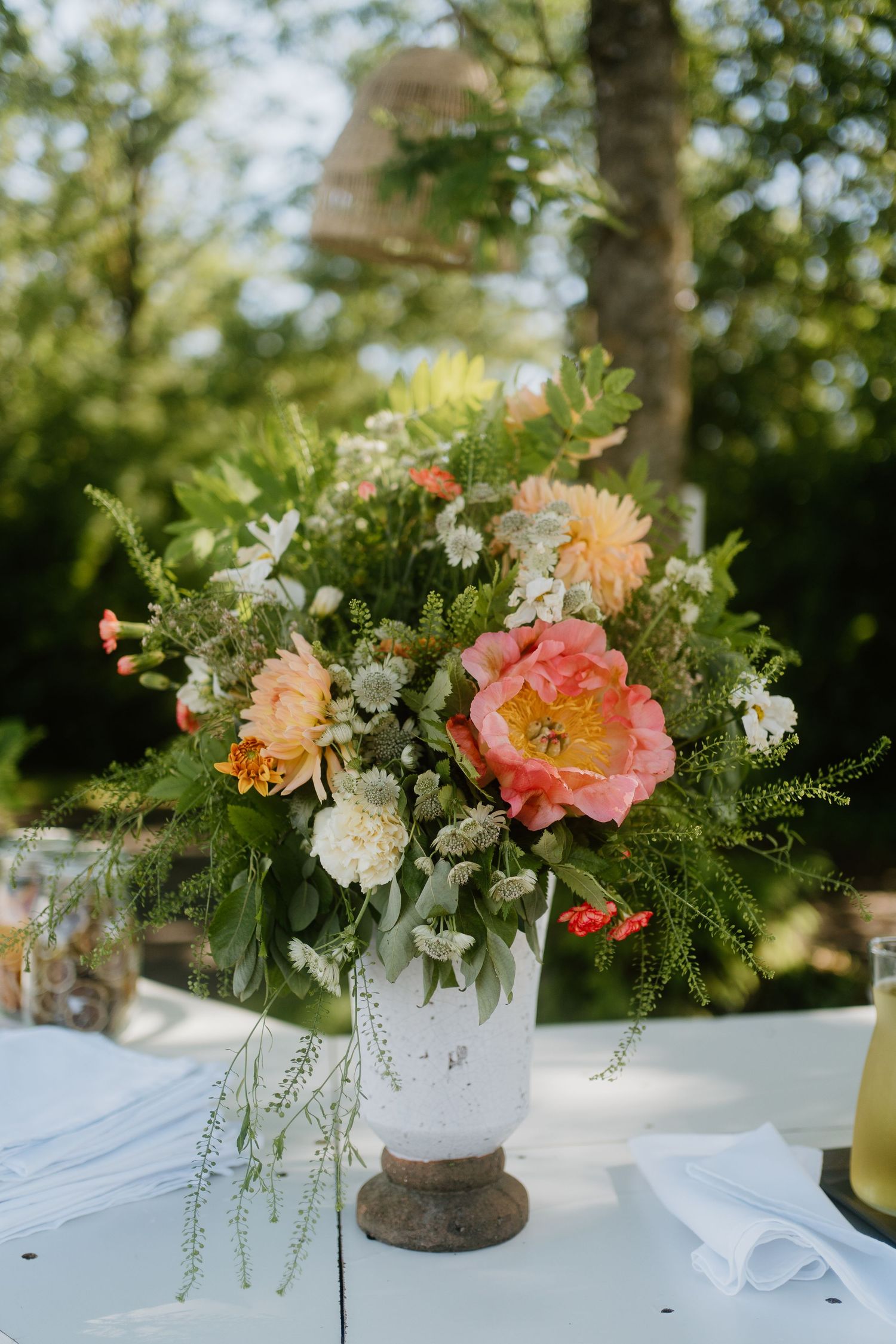 Elegant floral centerpiece with pink peonies and orange dahlias in rustic vase at outdoor wedding.