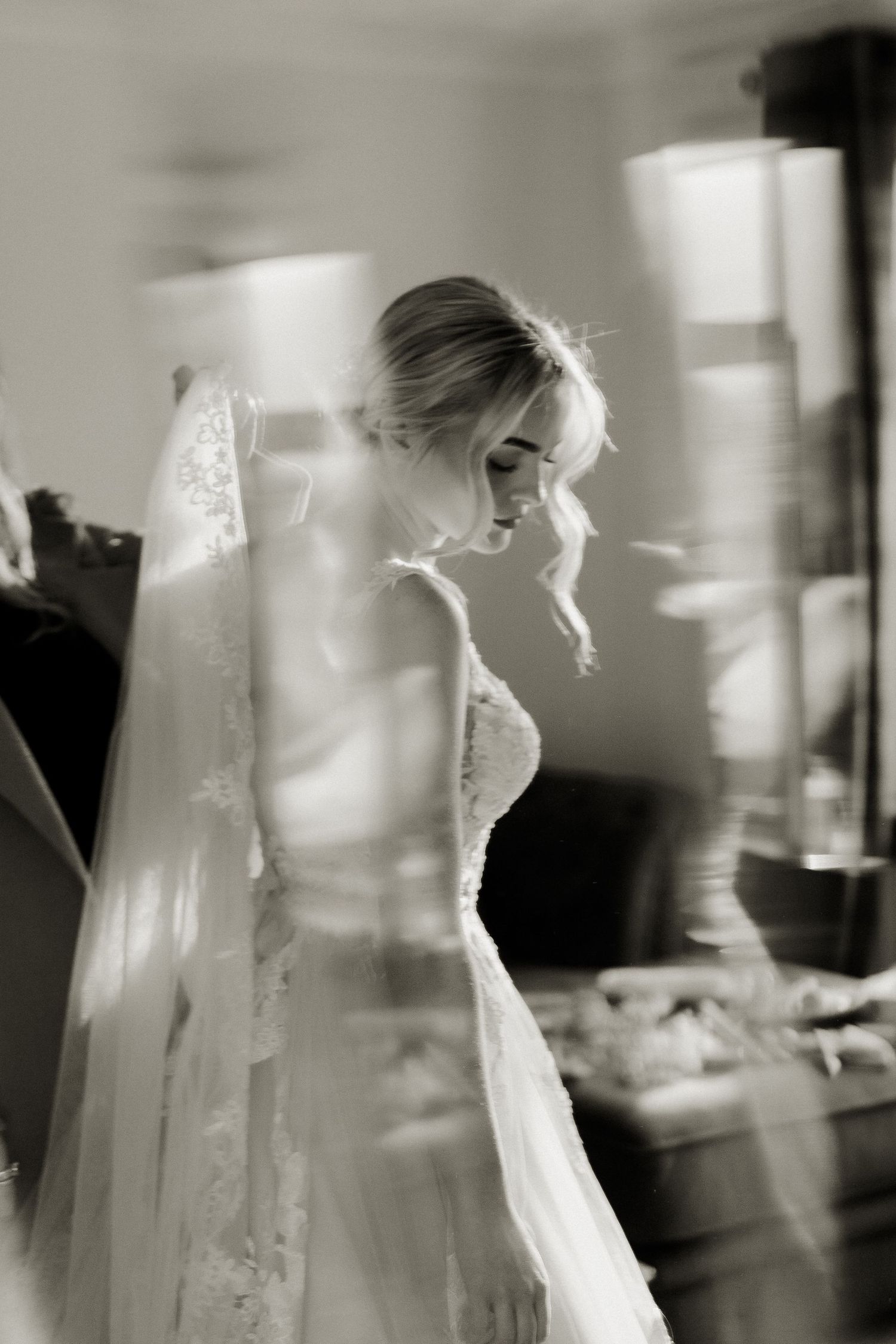Black and white photo of a bride in lace wedding dress and veil looking down elegantly.