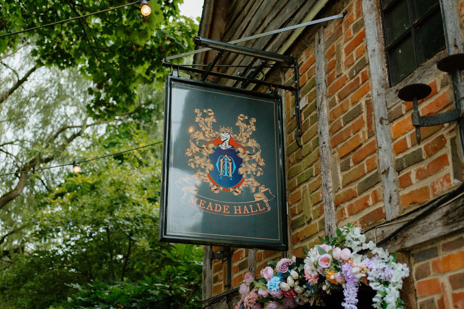 Elegant heraldic crest sign for Meade Hall venue mounted on a rustic brick wall with flowers.