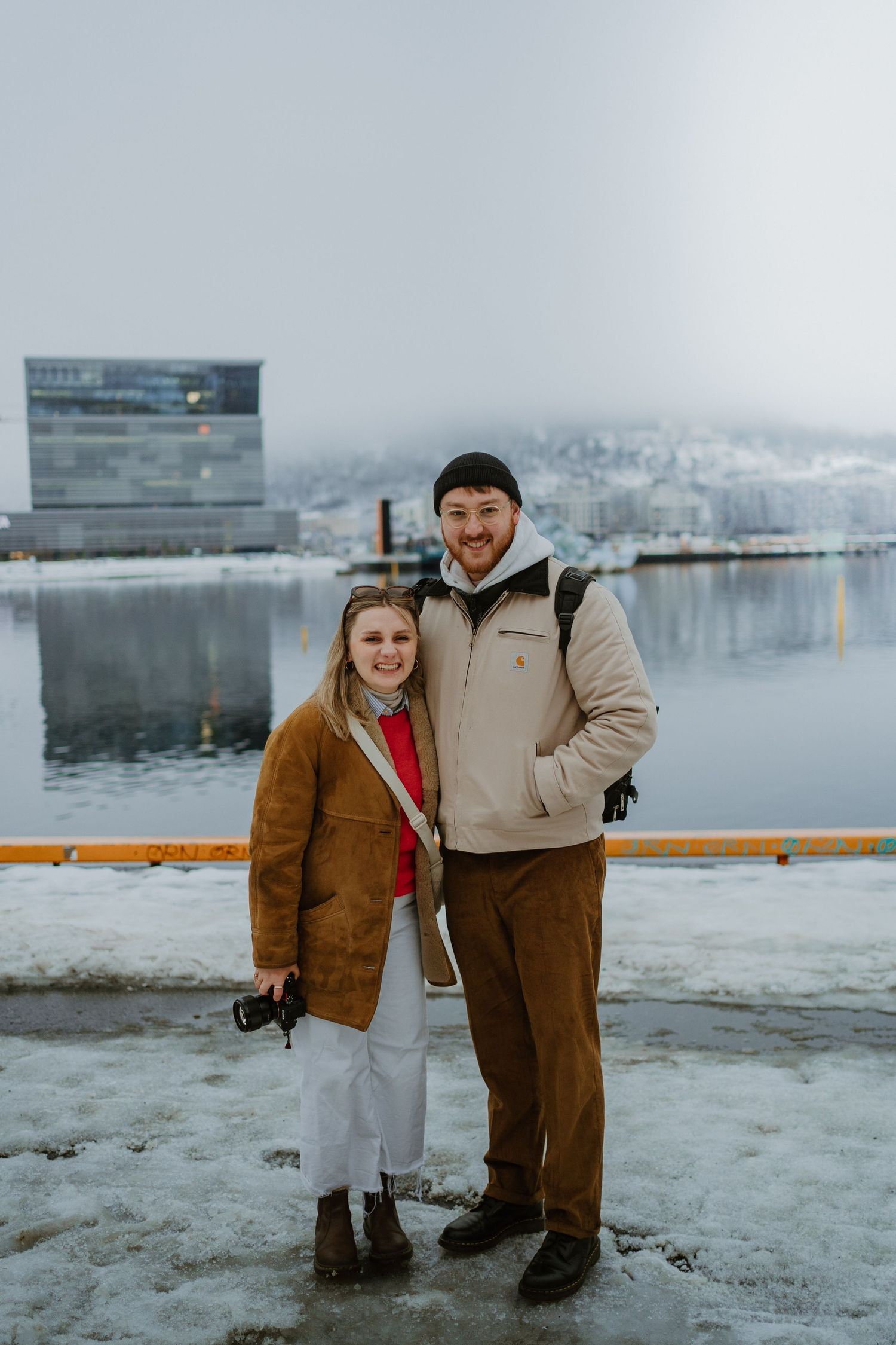 Winter scene with snowy harbor and modern building in background.