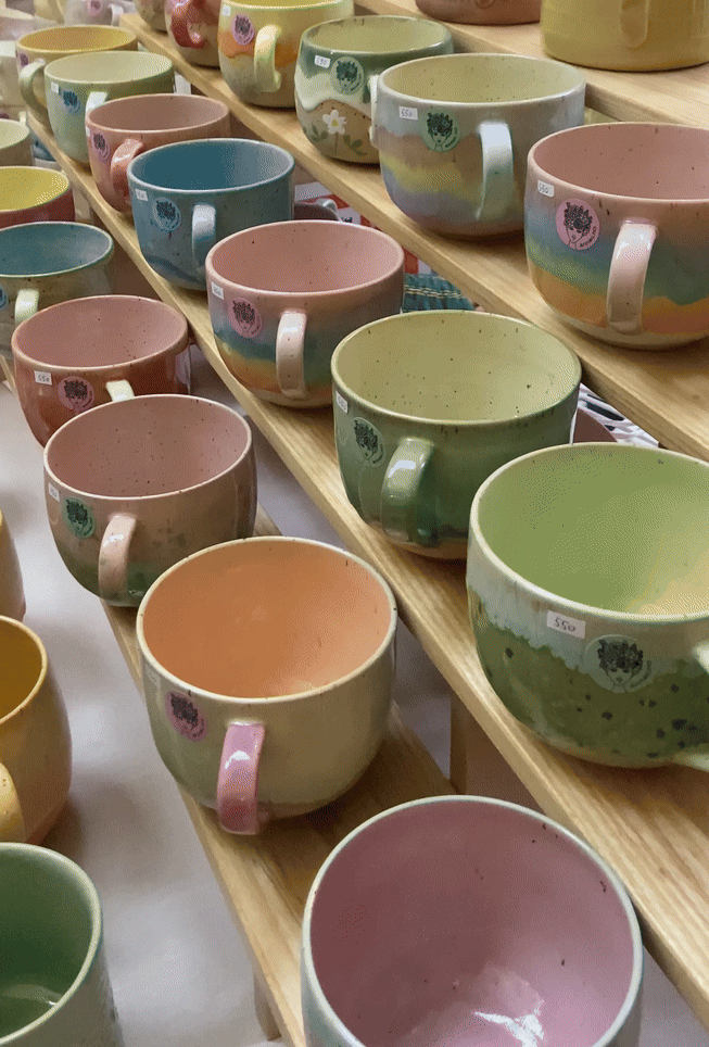 Handcrafted ceramic mugs in pastel colors of pink, green, and blue arranged in rows on a wooden surface.