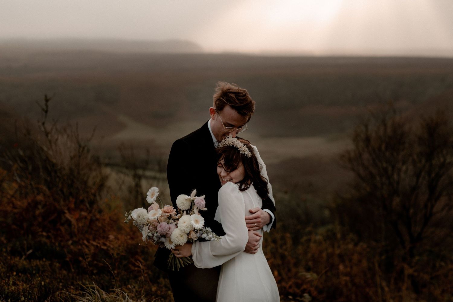 Wedding couple shares a tender embrace against a misty hillside backdrop.