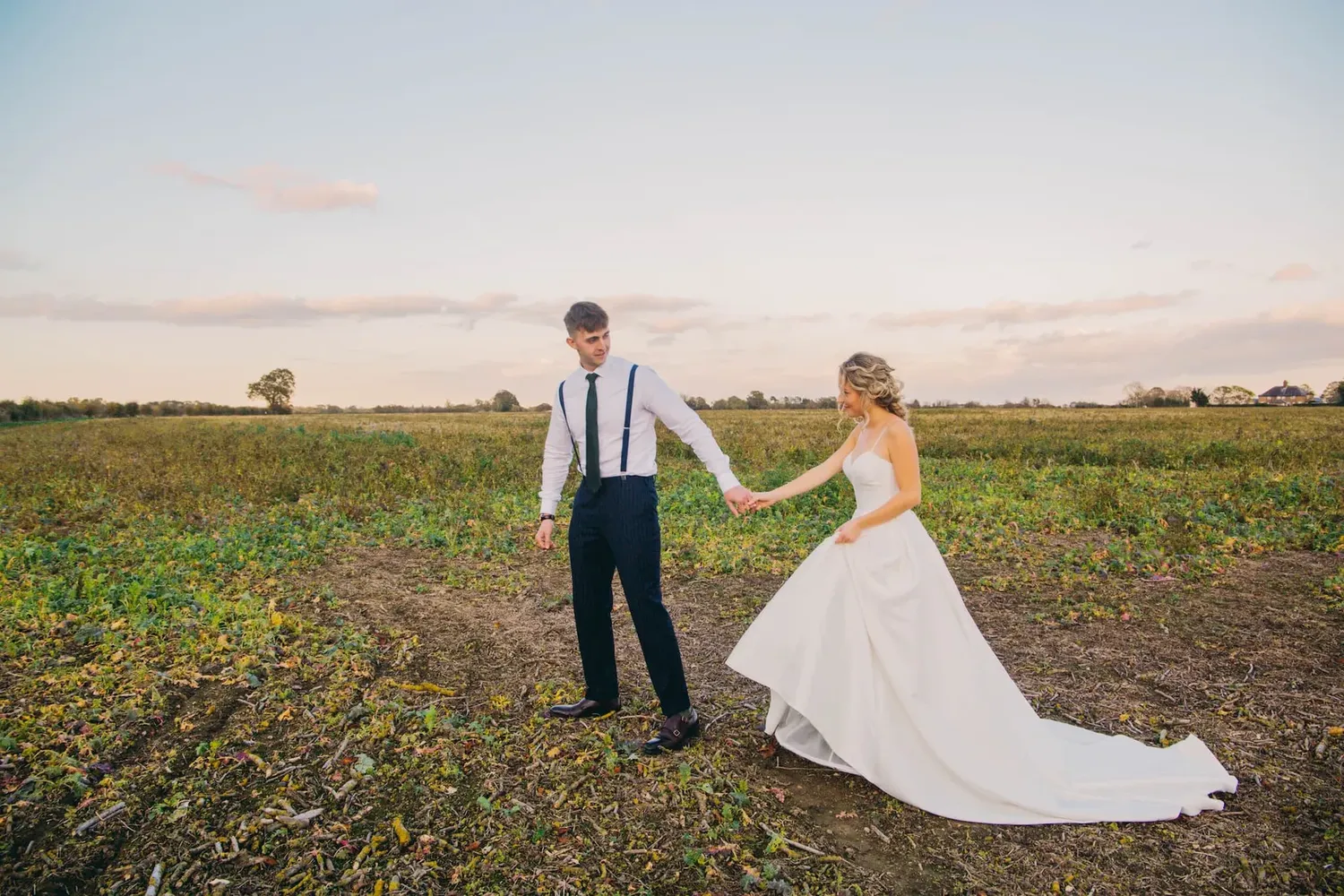 A couple holds hands in a field during golden hour.