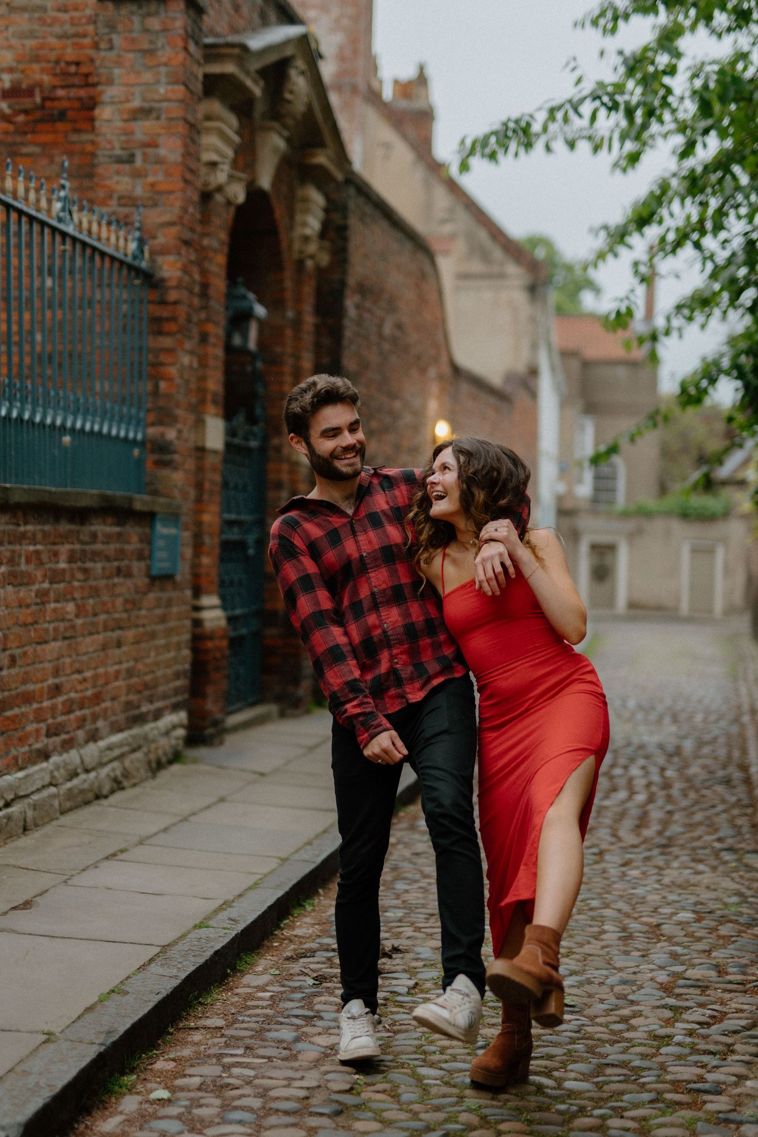Smiling couple walking arm in arm along a historic cobblestone street with brick walls.