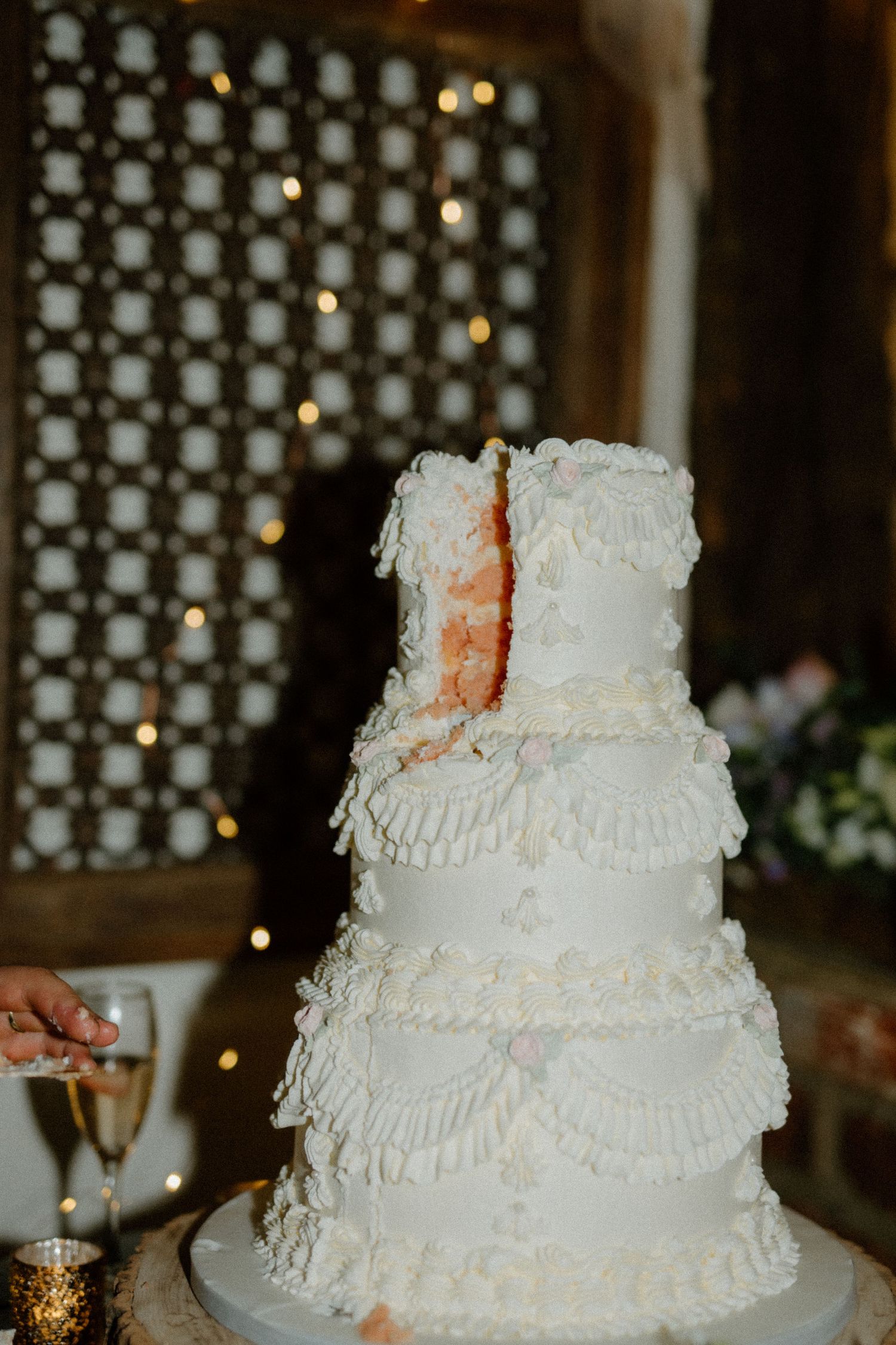 Elegant white tiered wedding cake with delicate lace-like frosting details and soft coral accents displayed at reception venue.