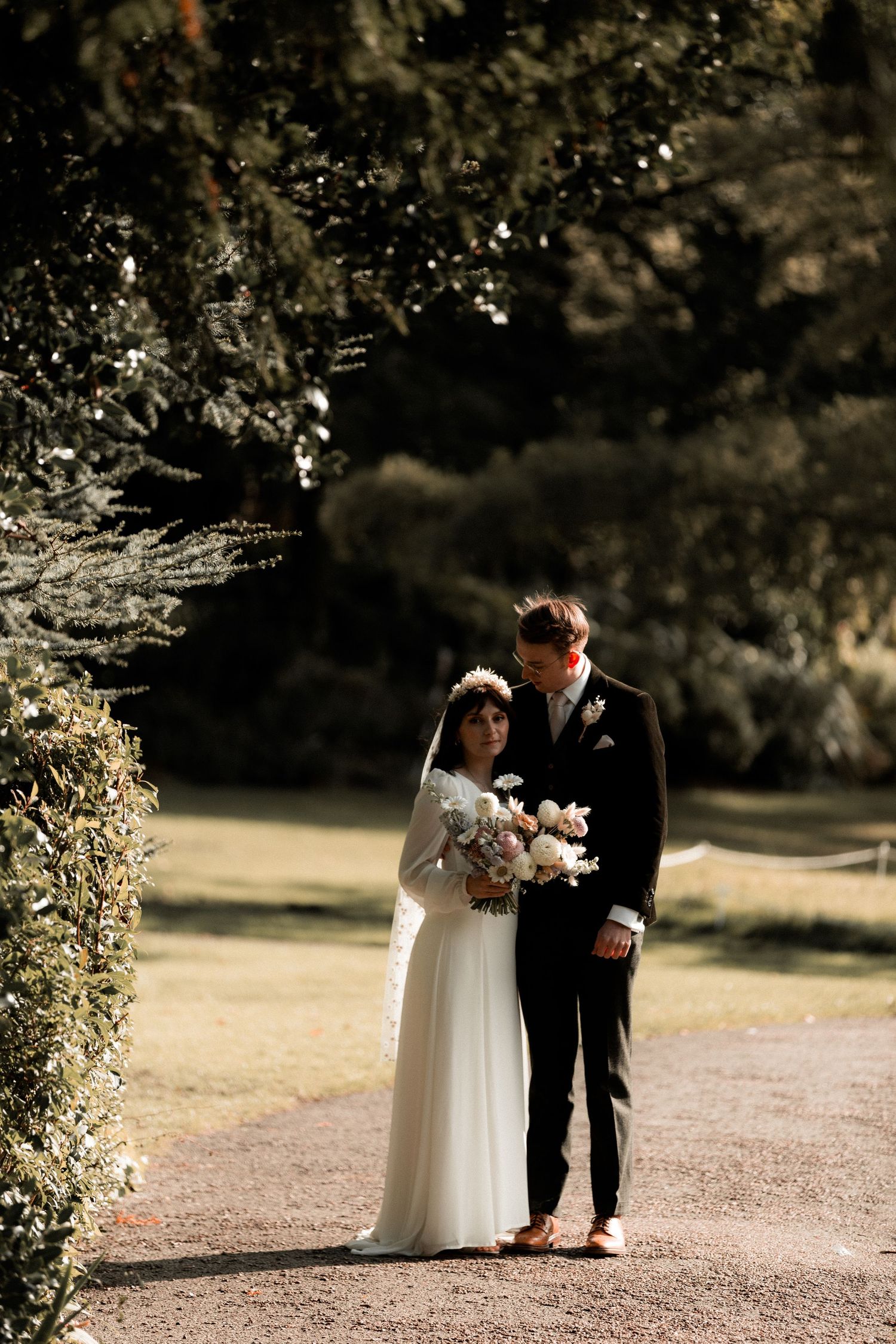 Newlyweds pose together on a garden path surrounded by lush greenery.