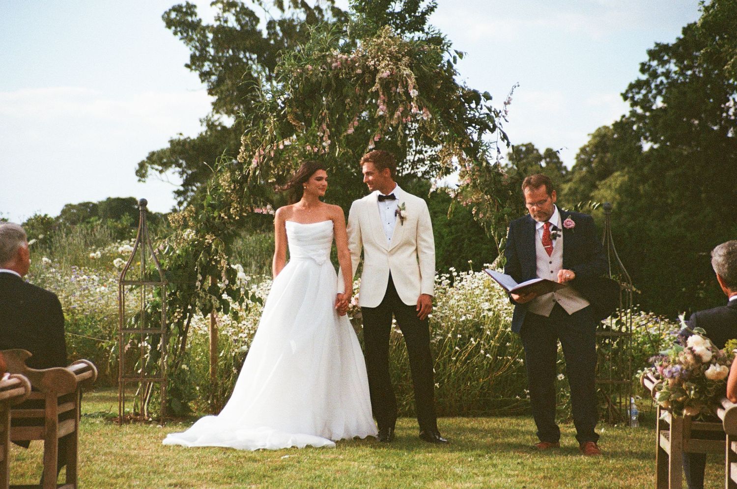 Couple exchanging vows outdoors with officiant at garden wedding ceremony.