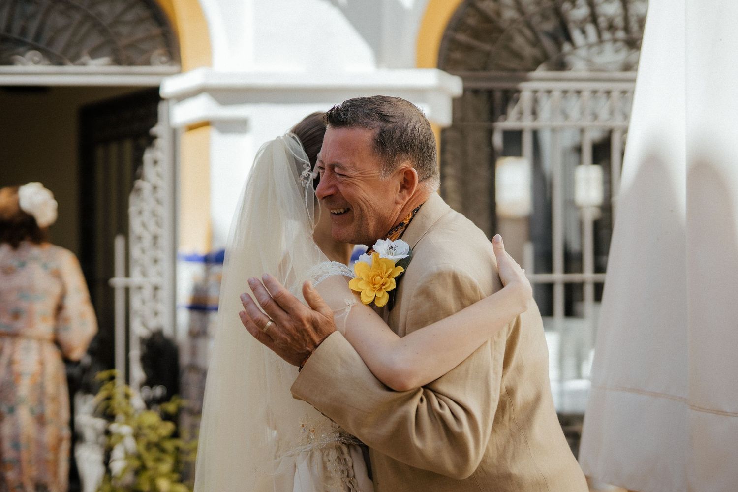 Emotional father of the bride sharing warm embrace with daughter in wedding dress and veil.
