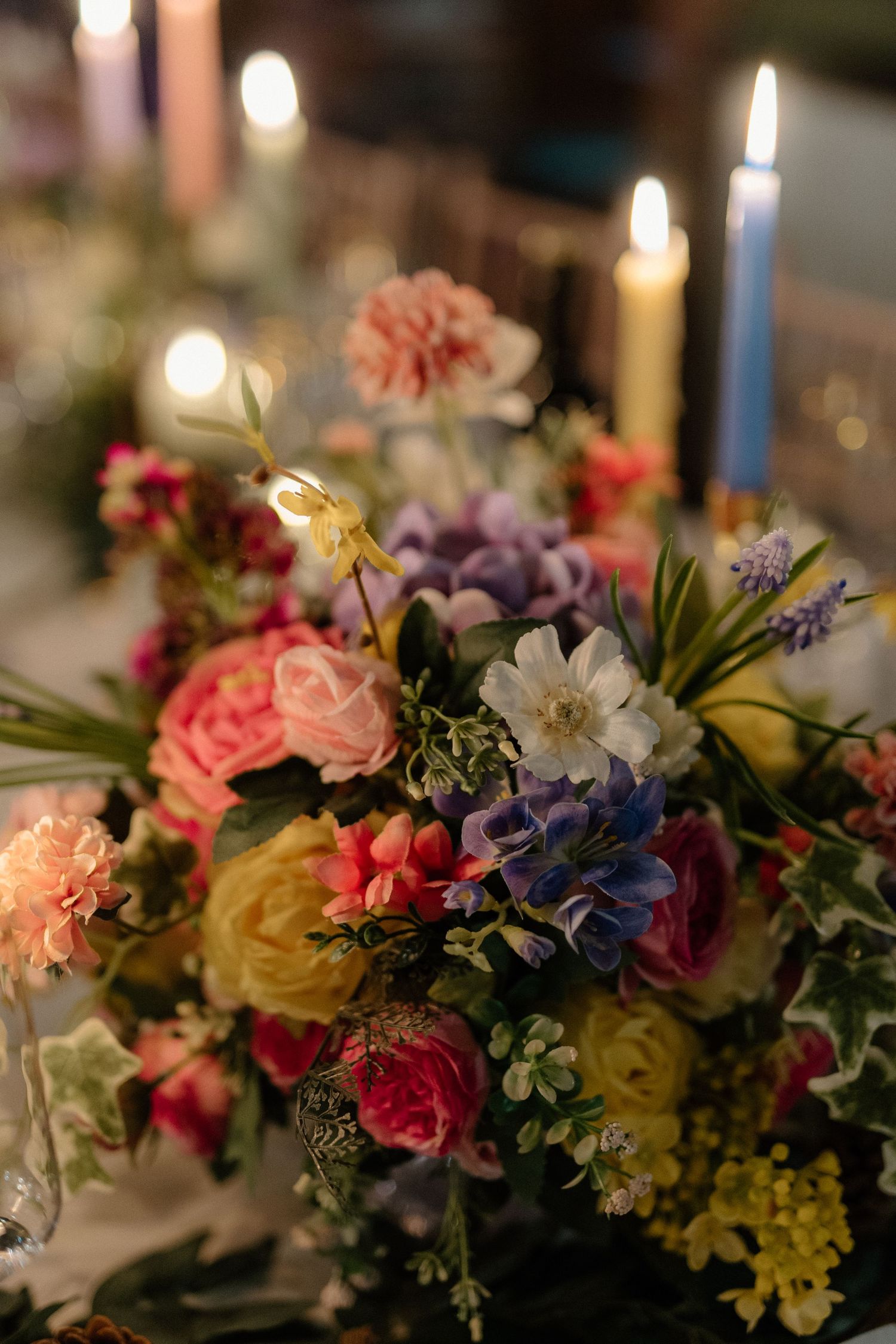 Romantic floral centerpiece with colorful roses, carnations and lit candles creating an elegant table setting.