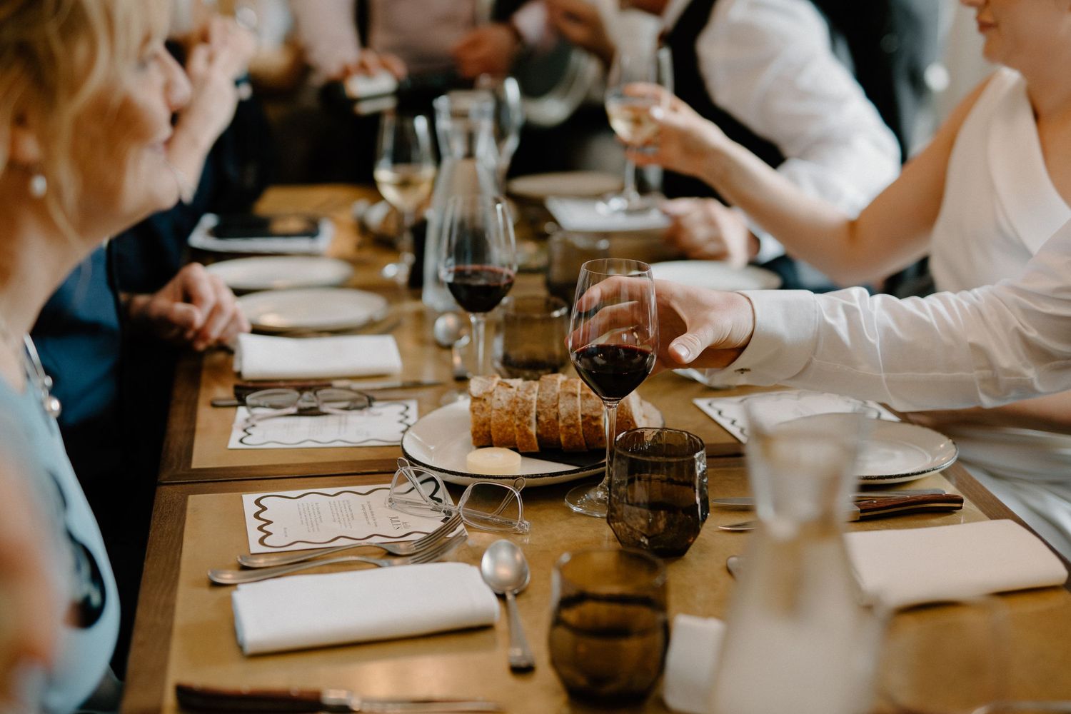People enjoying wine and conversation around a table setting with wine glasses and place settings at a restaurant.