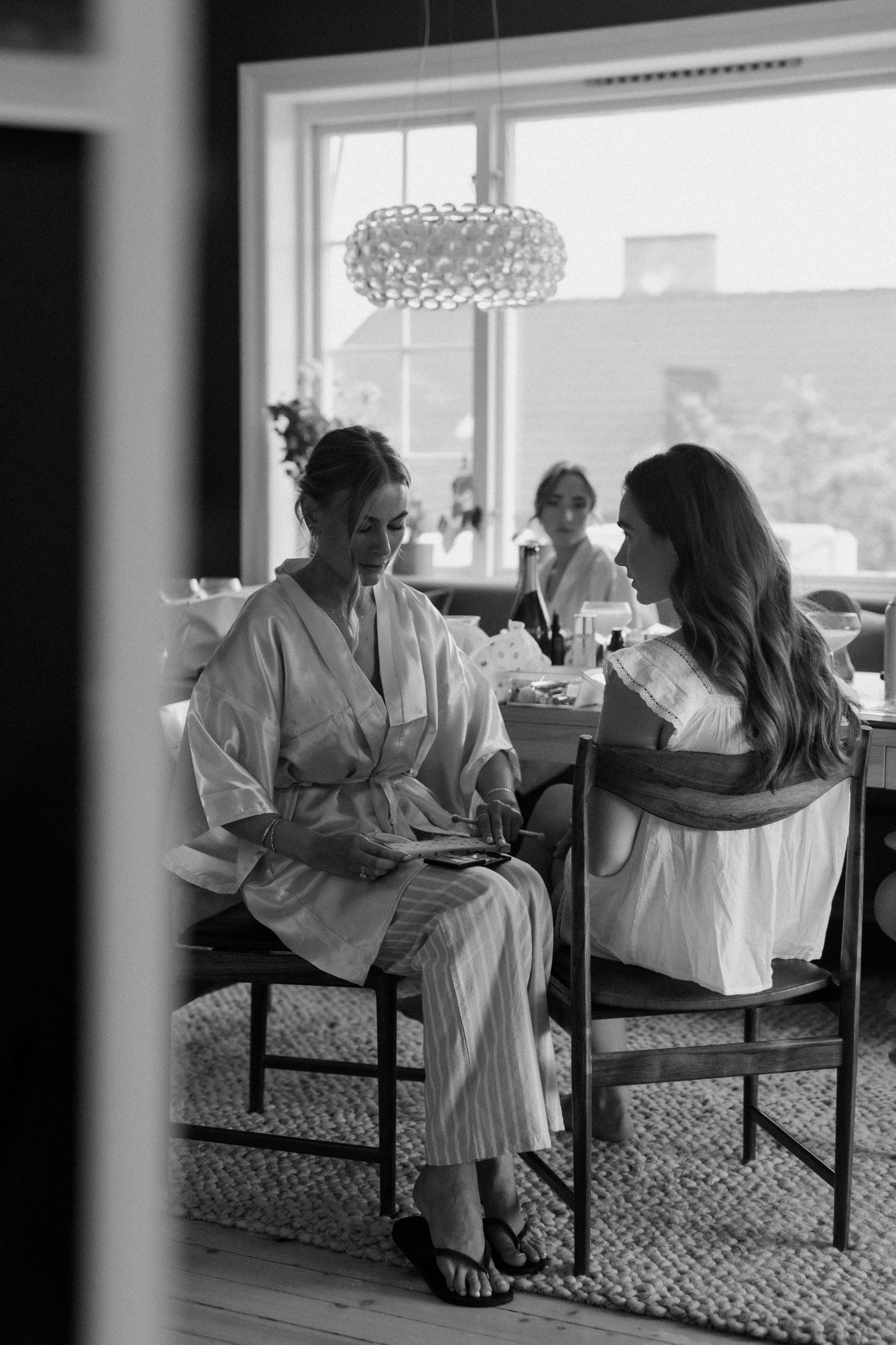 Black and white photo of bride and bridesmaid in robes chatting during wedding preparations.