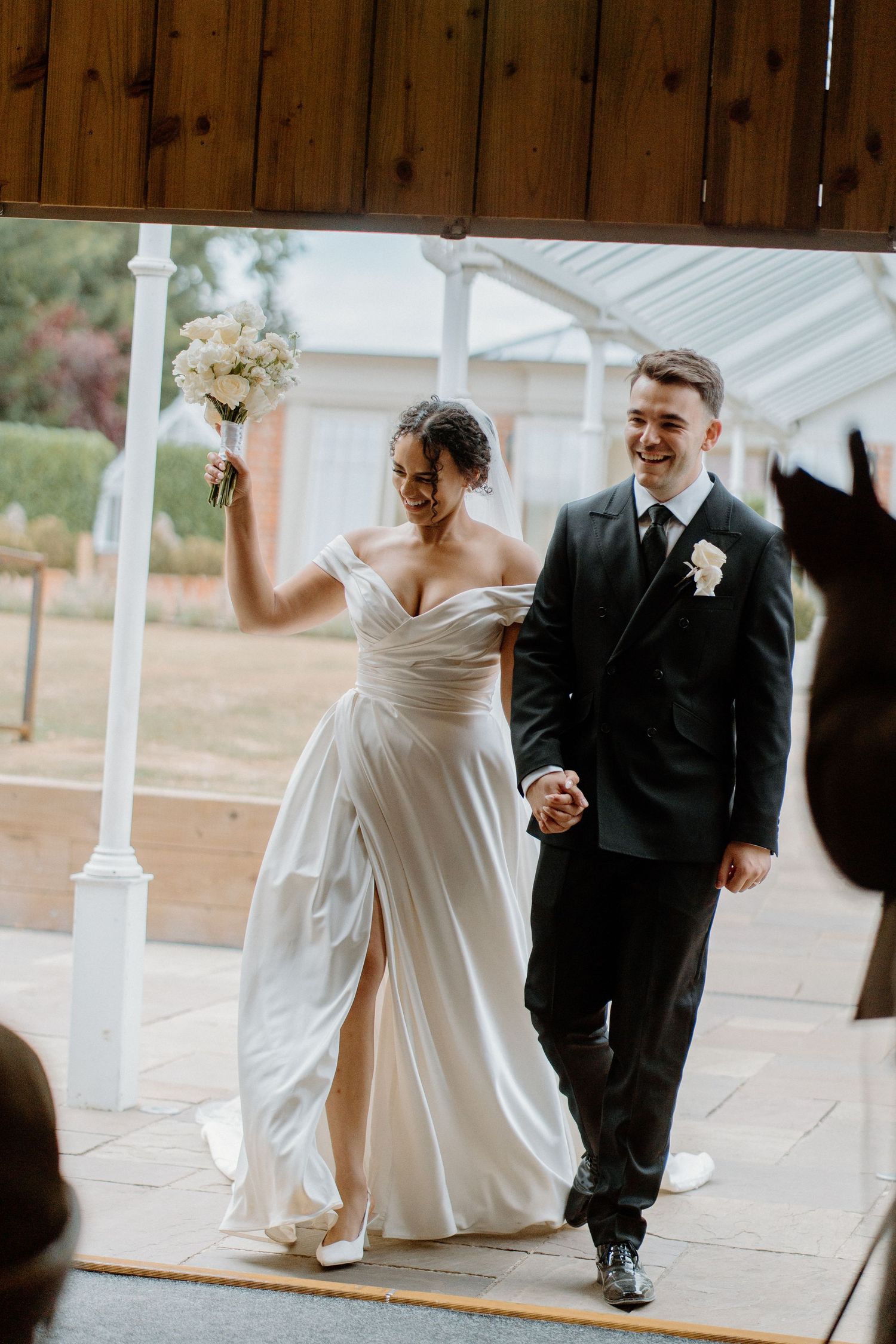 Joyful bride raises bouquet and groom smiles as they walk back down the aisle after ceremony.