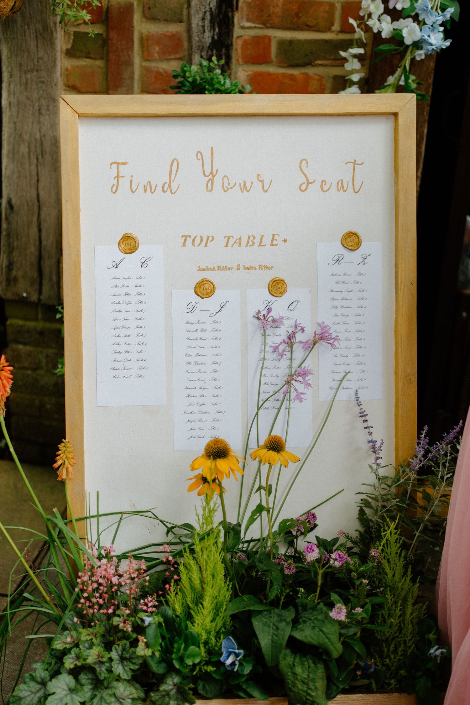Elegant wedding seating chart in a wooden frame surrounded by wildflowers and greenery.