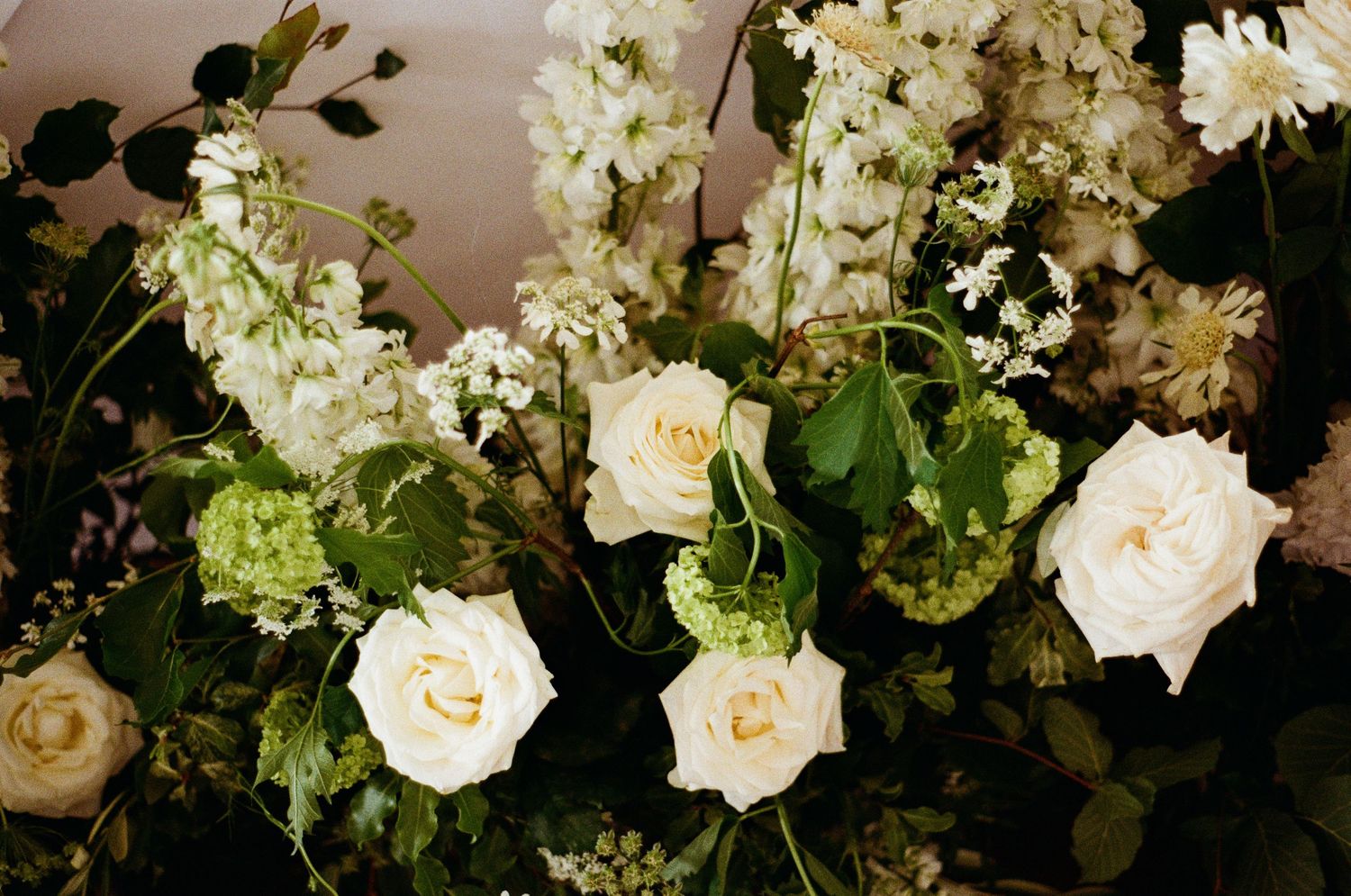 Lush wedding floral arrangement featuring white roses, green hydrangeas, and delicate blooms on dark background.