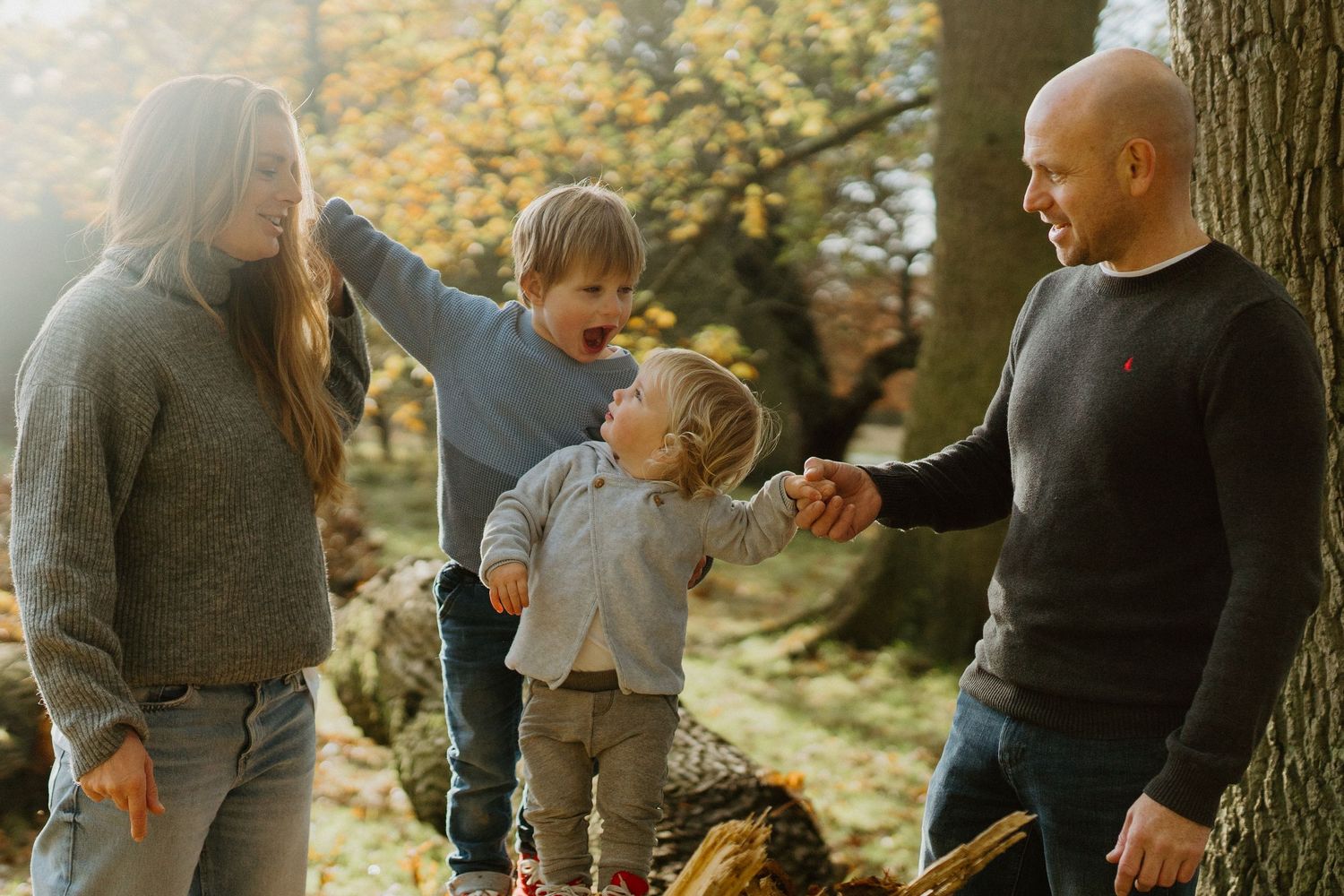 Family of four enjoying a sunny autumn day outdoors among colorful fall foliage.