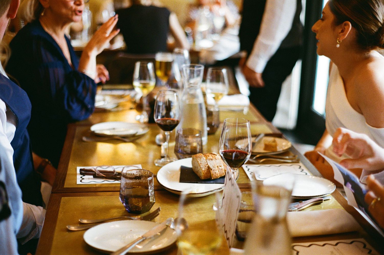 Guests dining at elegantly set wooden table with wine glasses at wedding reception.