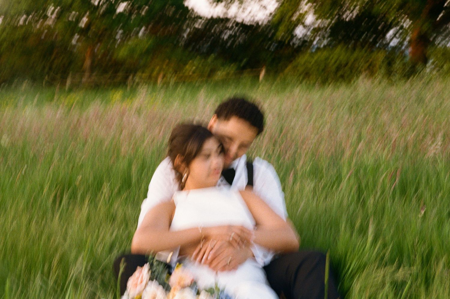 Blurry romantic photo of bride and groom embracing in a lush green meadow field.